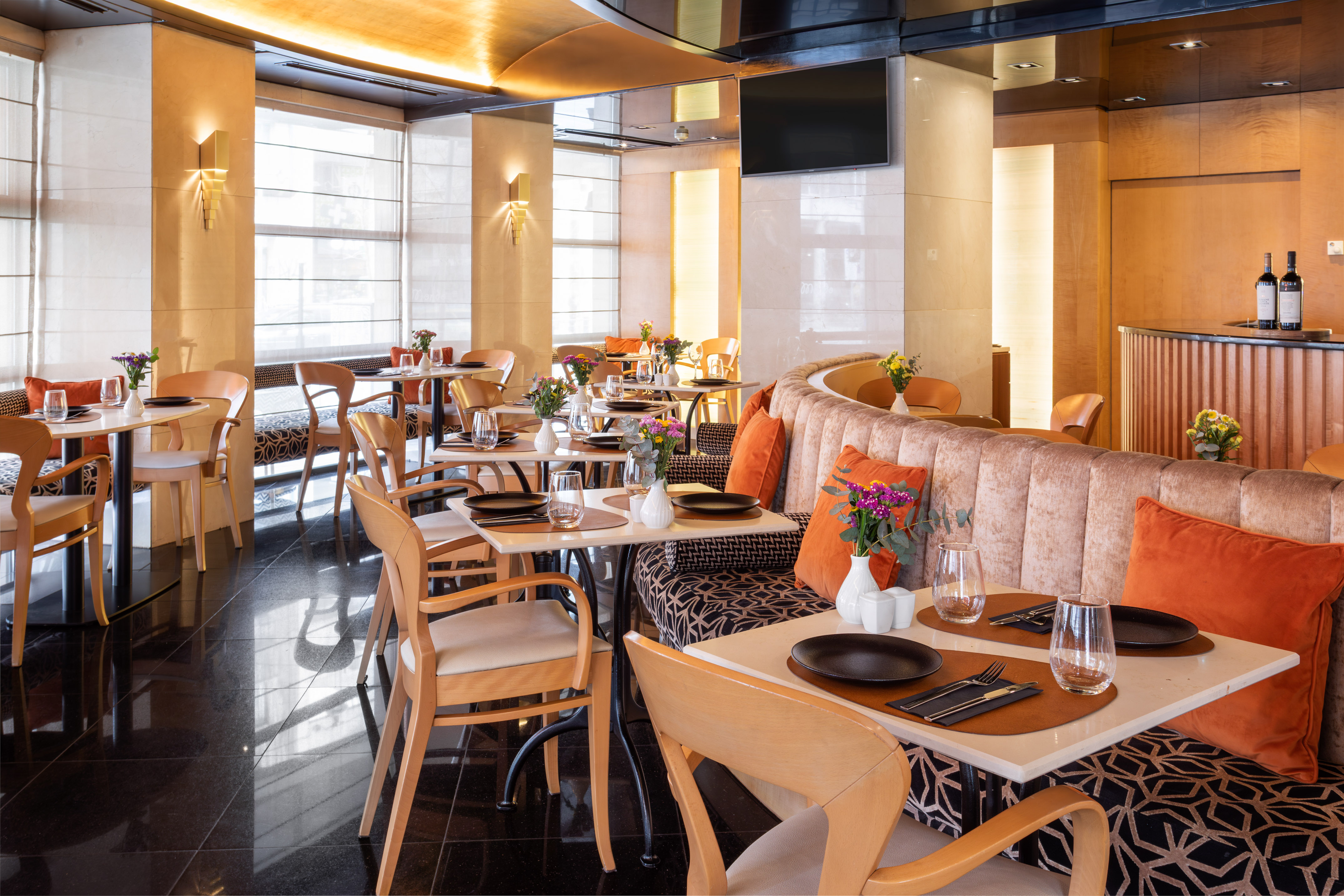 Modern restaurant dining room with set tables, banquette seating, and bright windows.