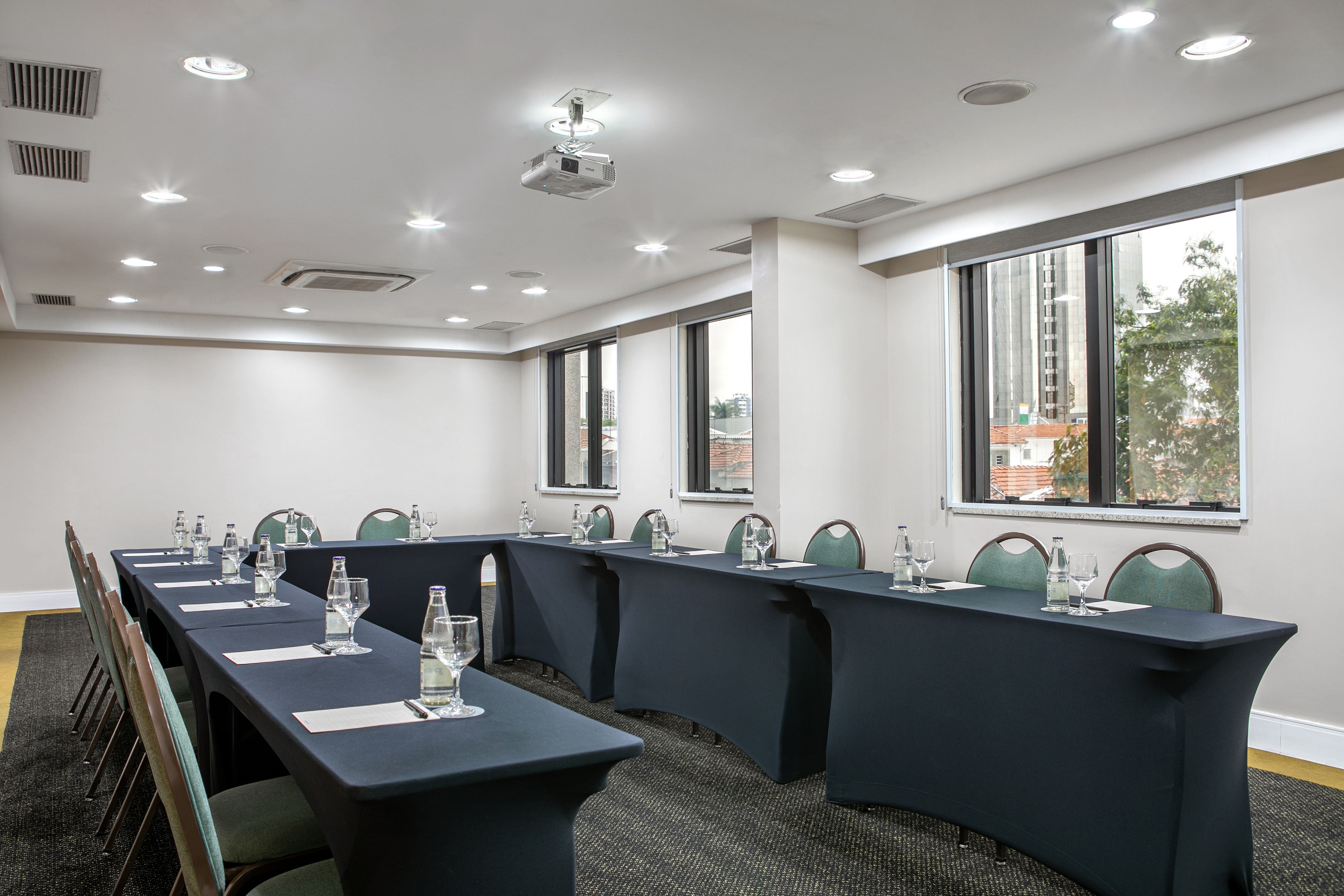 U-shaped corporate meeting room with projector, black tables, and green chairs.