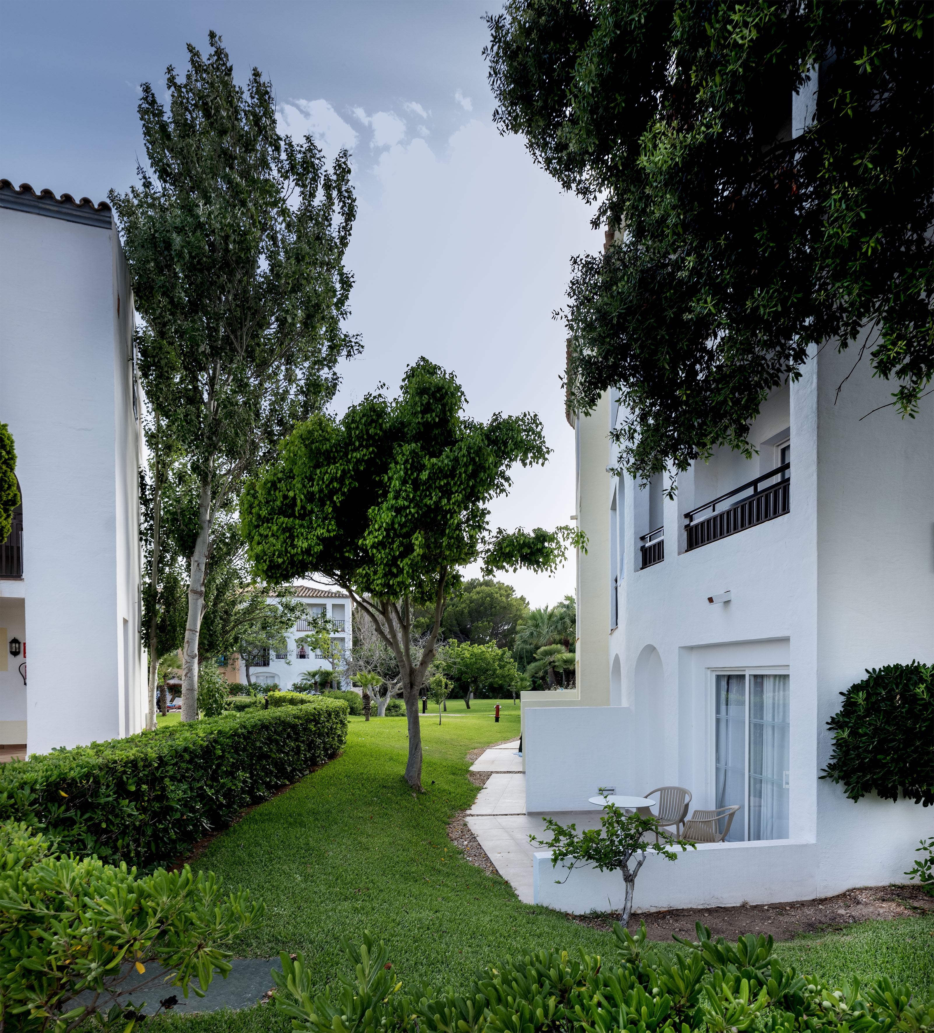 White hotel buildings with green garden, trees, and outdoor patio areas.