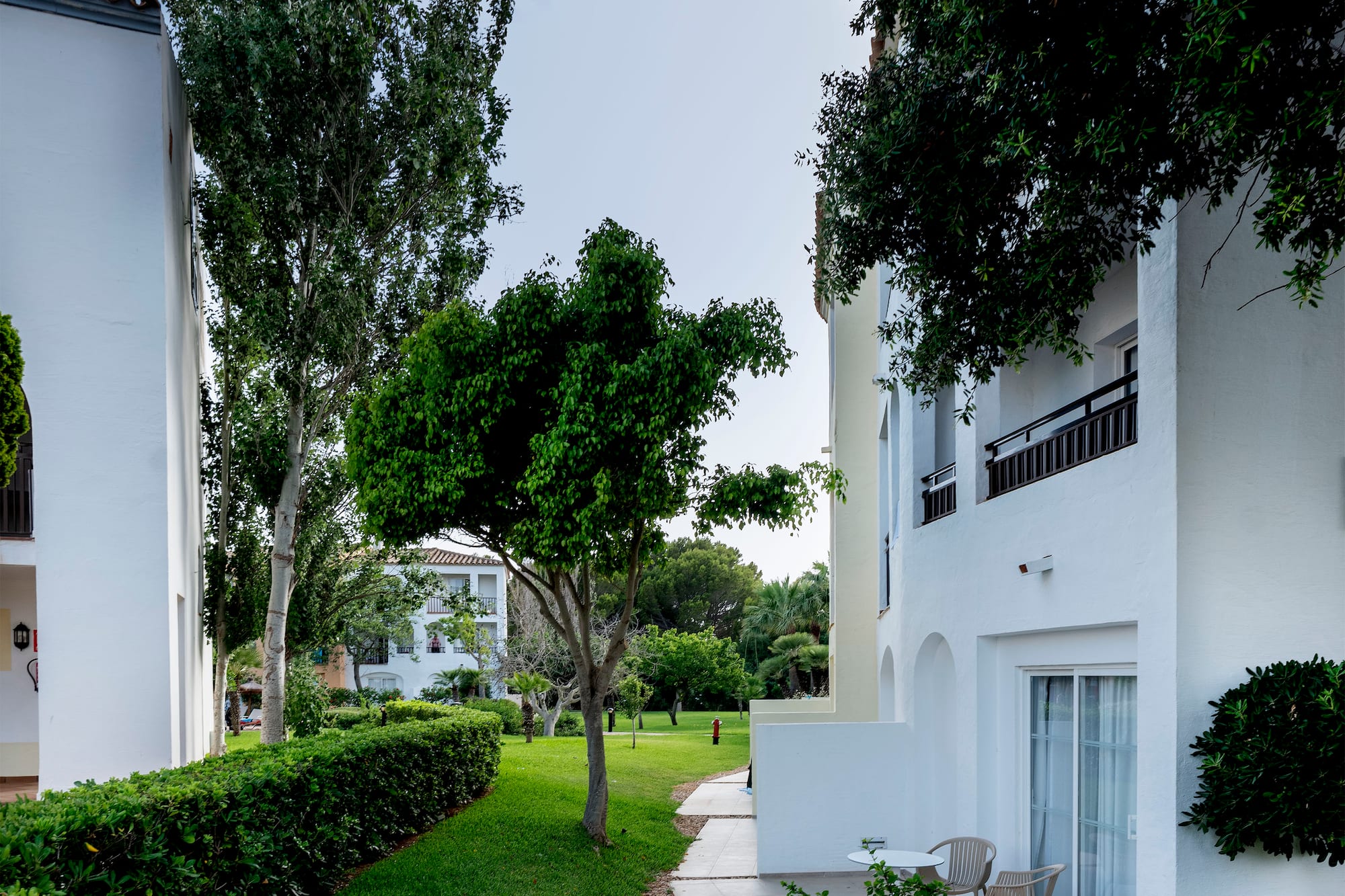White hotel buildings with green garden, trees, and outdoor patio areas.