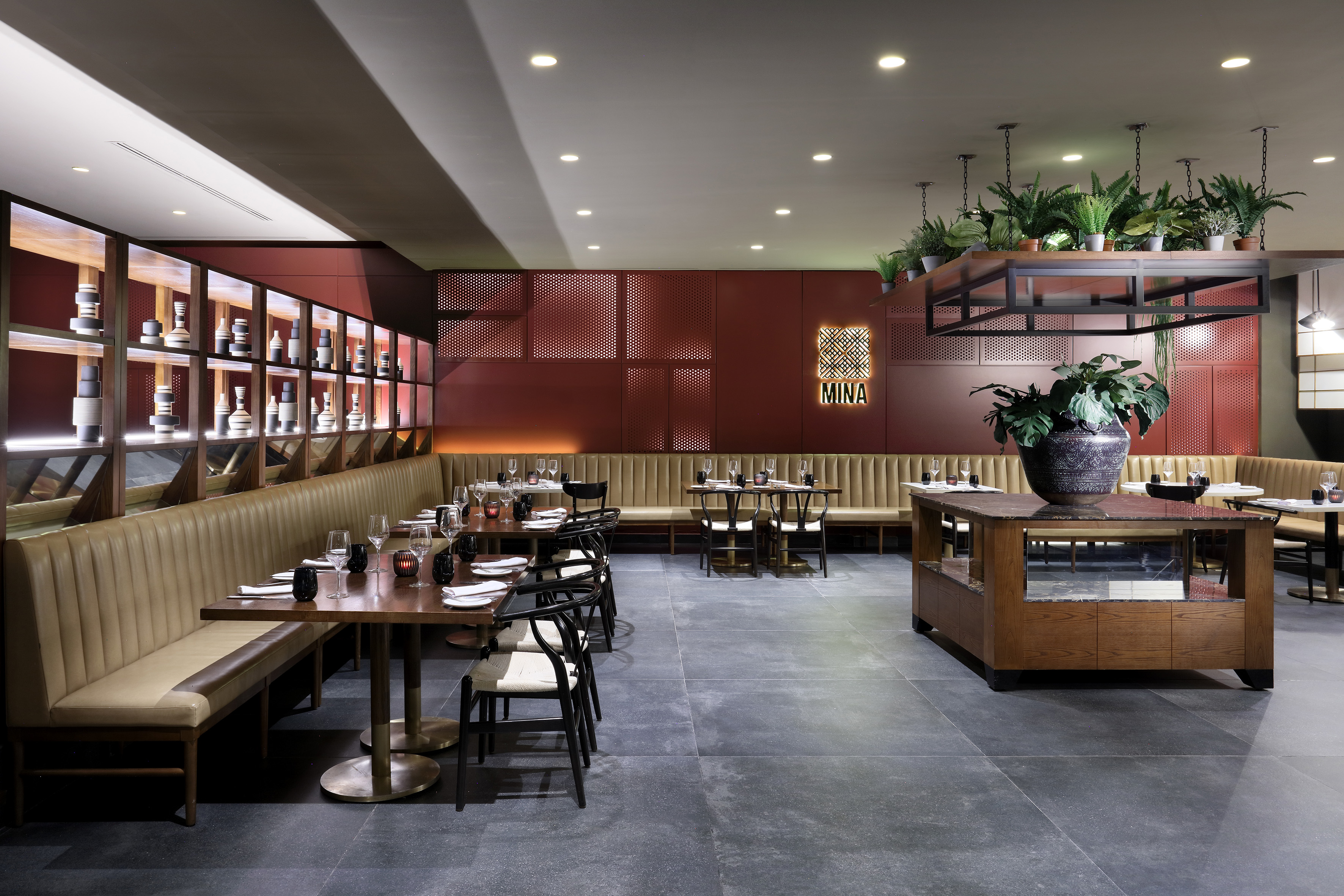Mina restaurant interior featuring red walls, booth seating, and hanging plants.