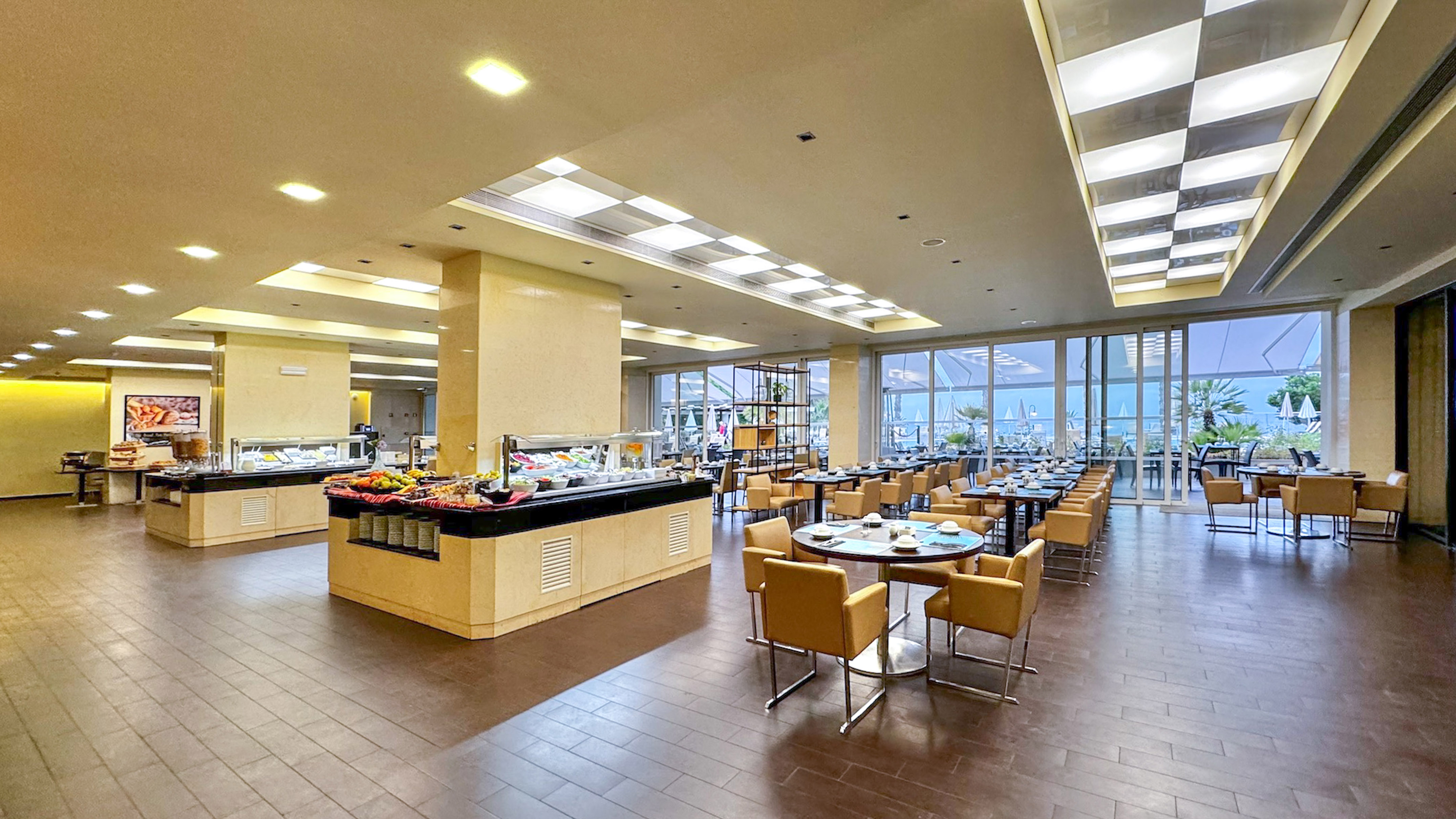 Spacious resort buffet with dining tables and sea view windows.