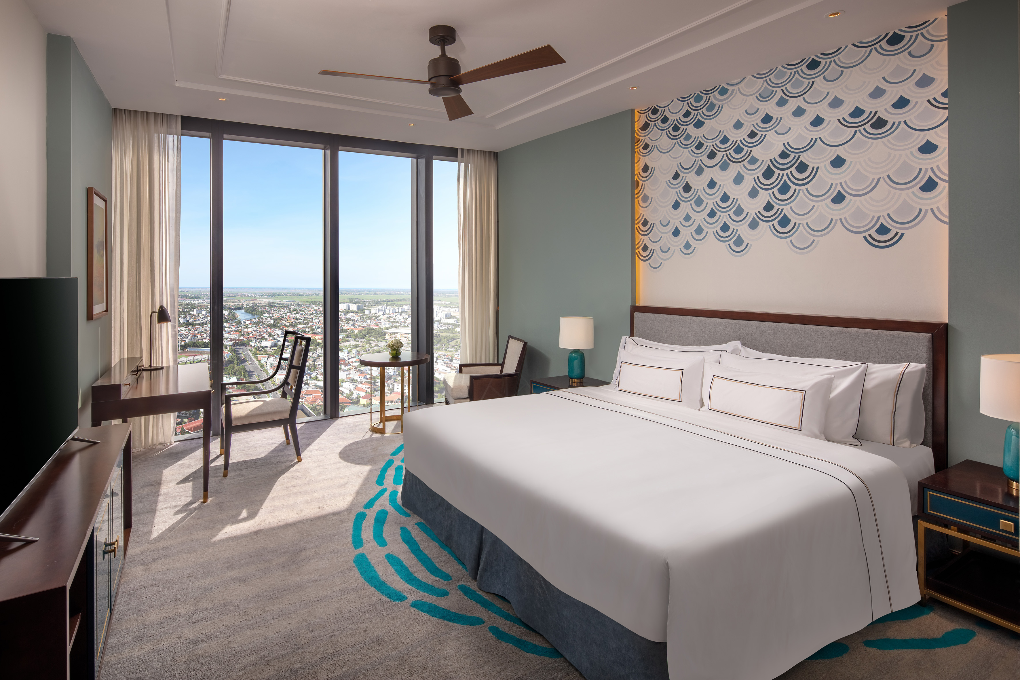 Modern hotel room with king bed, panoramic city and ocean view, elegant decor.