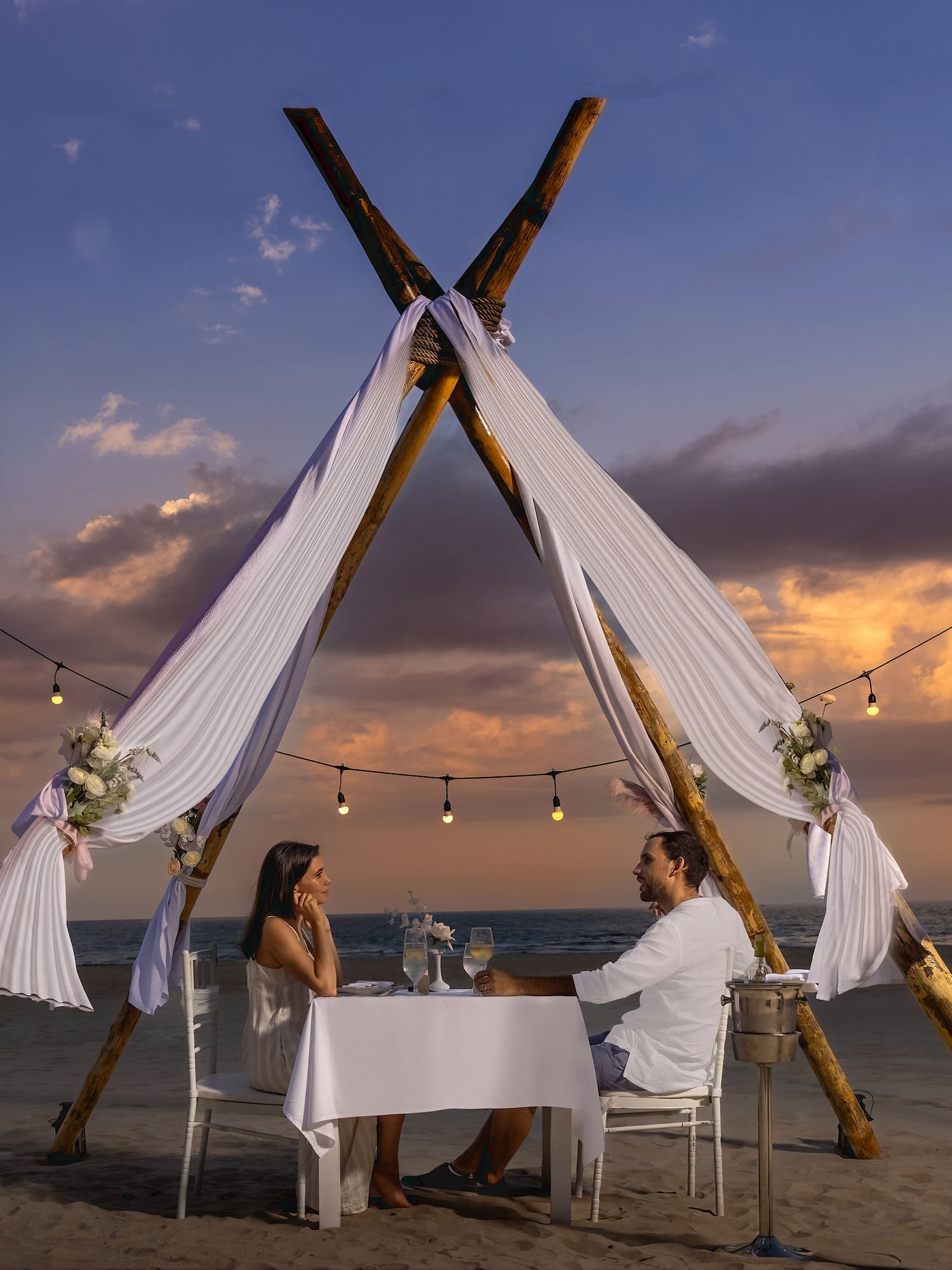 a man and woman sitting at a table on a beach