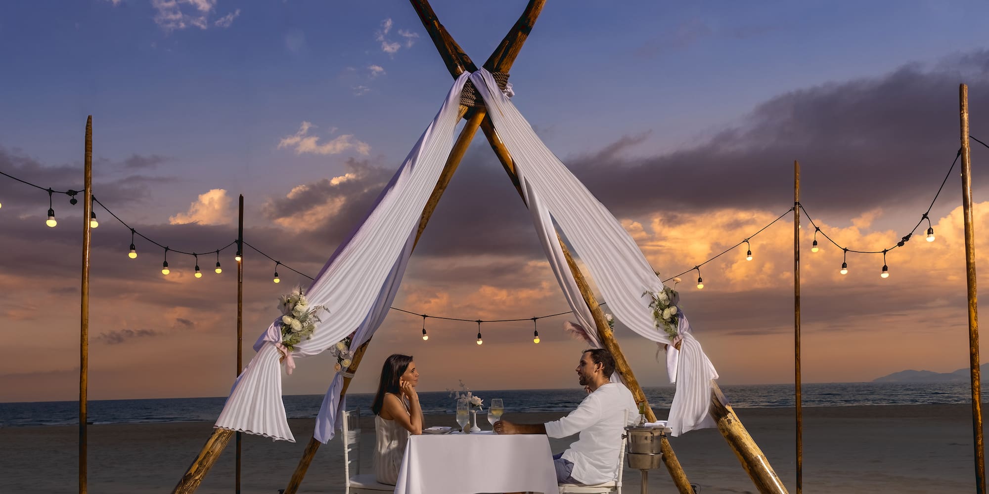 a man and woman sitting at a table on a beach