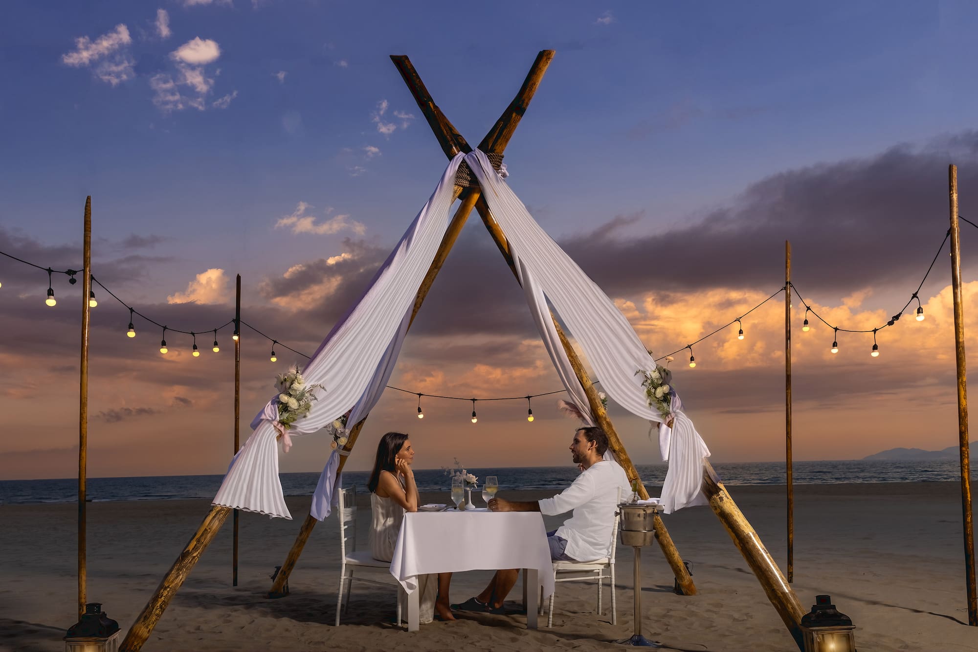 Romantic beach dinner for couple under teepee at sunset.