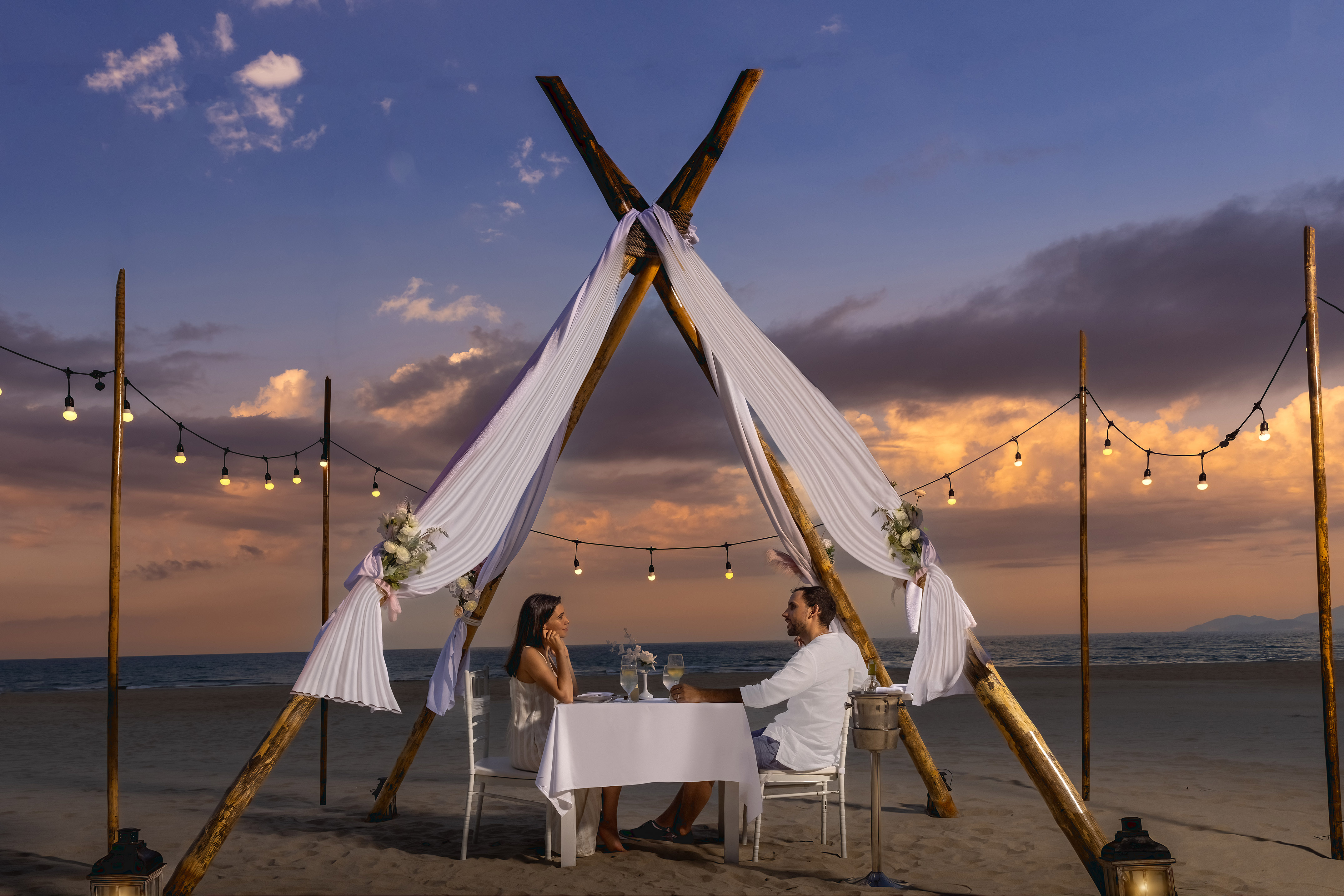 a man and woman sitting at a table on a beach