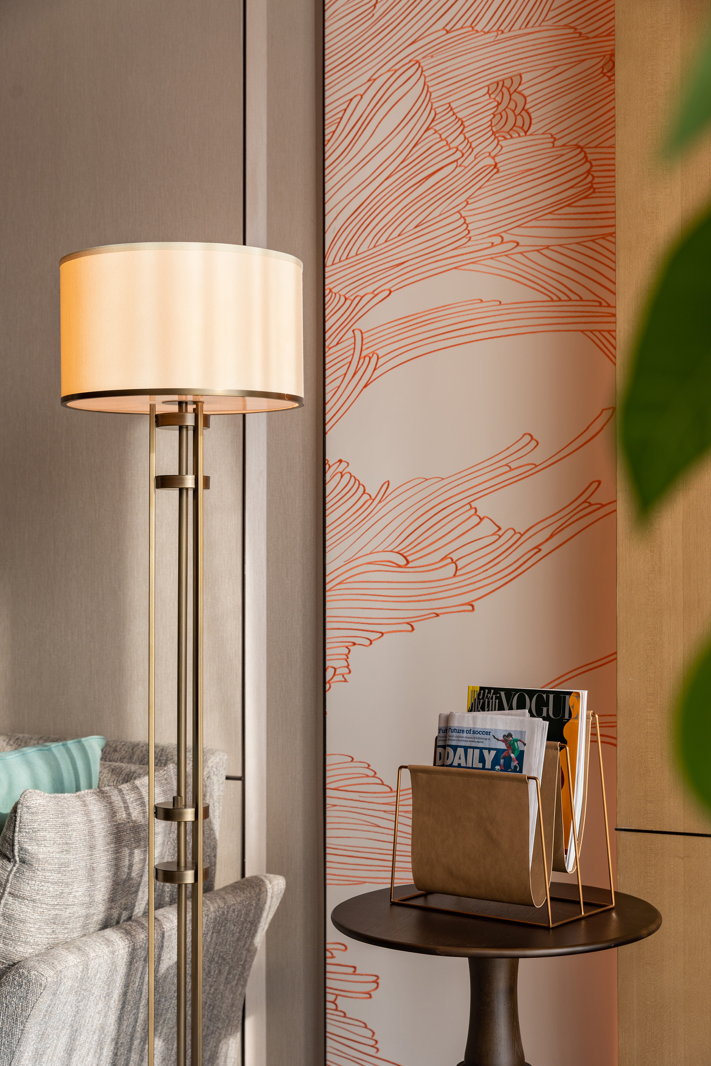Modern brass floor lamp, magazines on side table, patterned wallpaper.