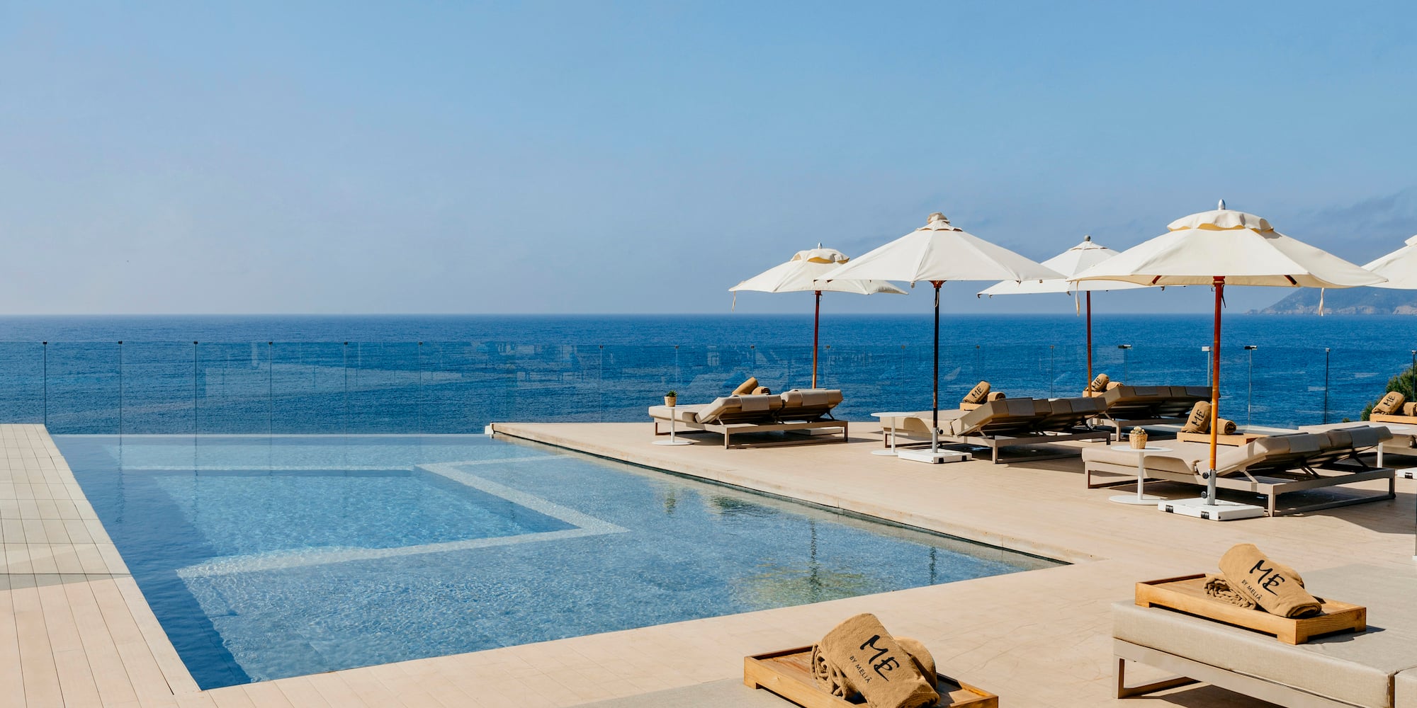 a pool with umbrellas and lounge chairs by the ocean