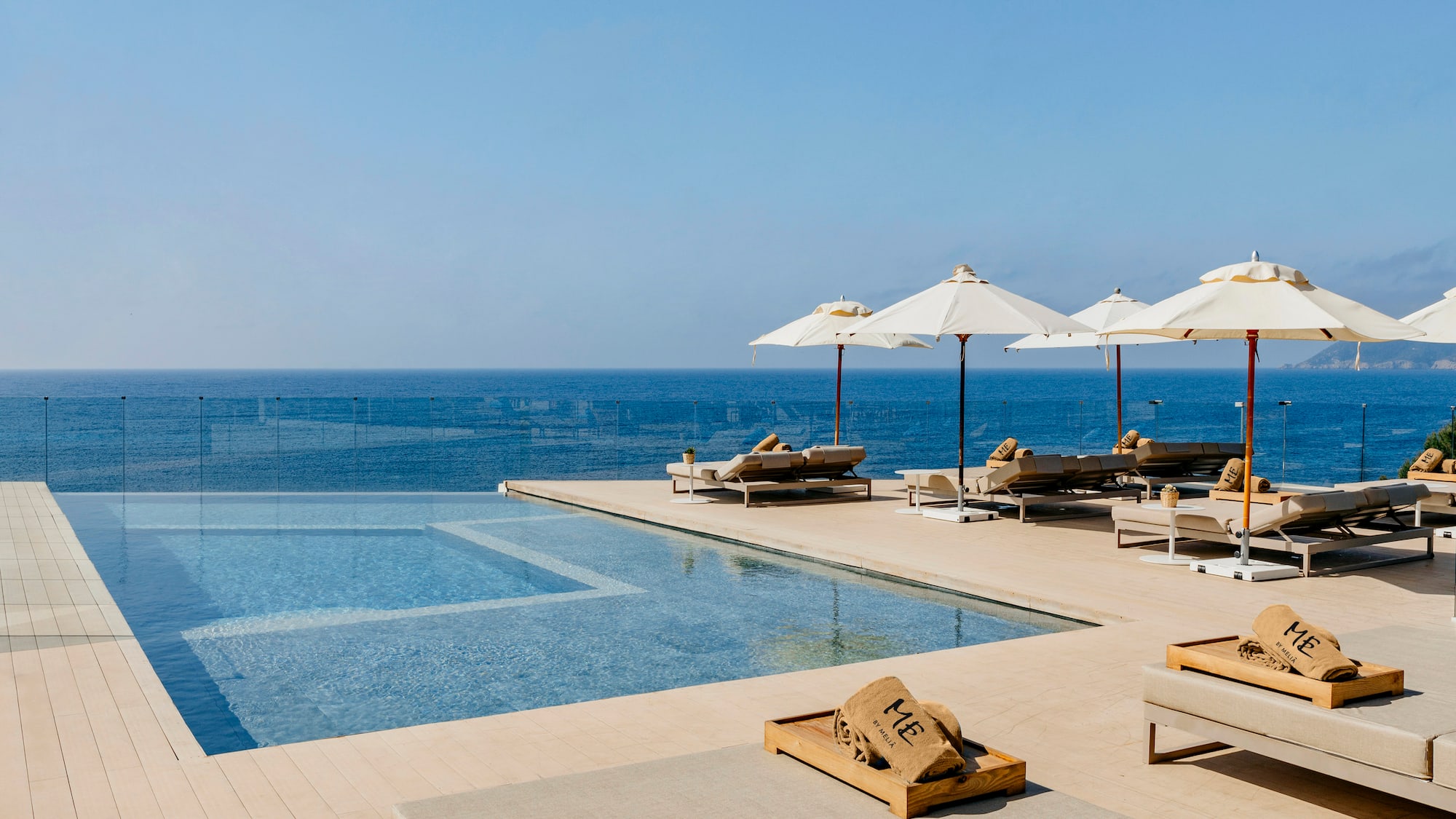 a pool with umbrellas and lounge chairs by the ocean