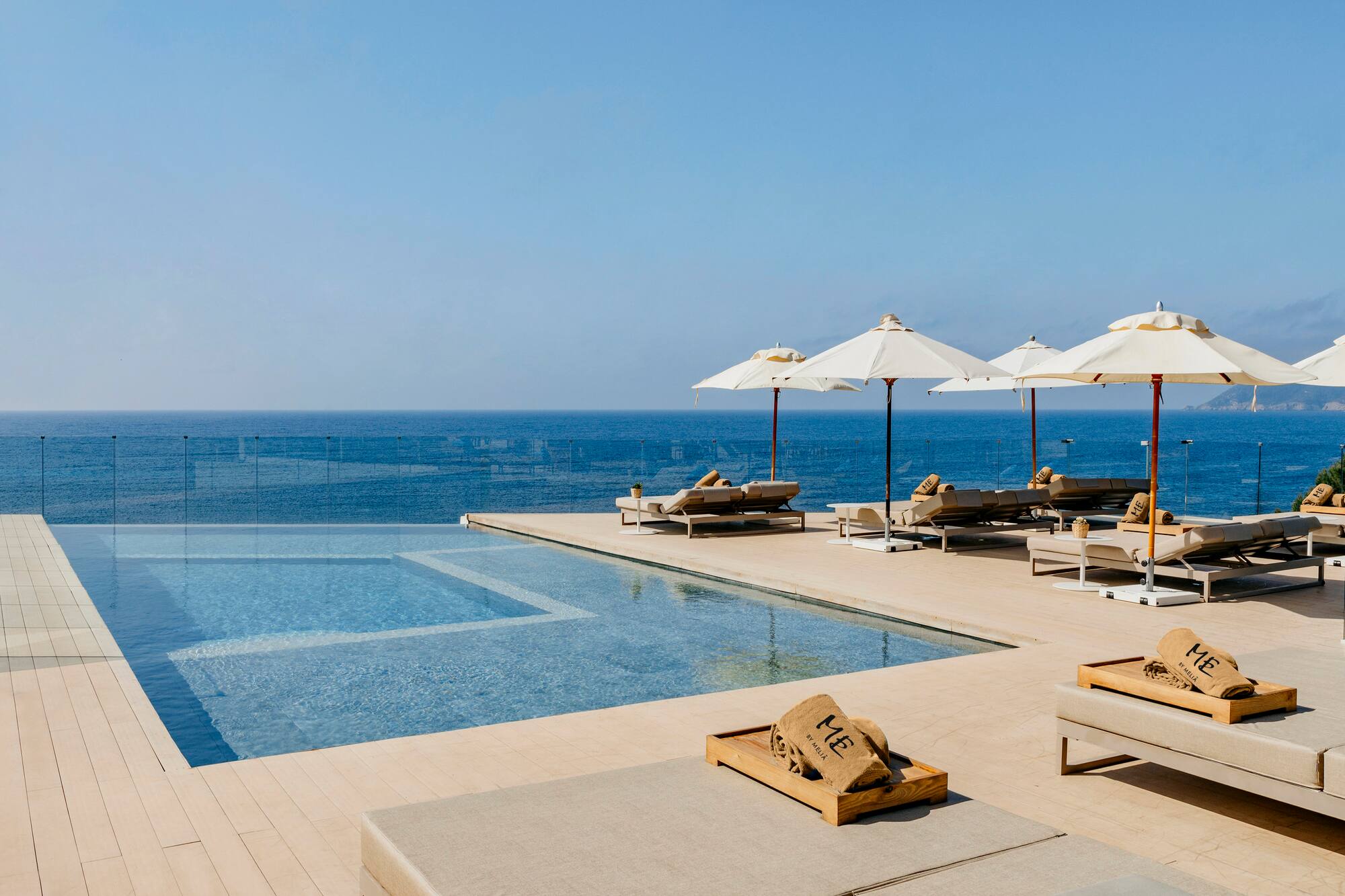 Luxury resort infinity pool with ocean view, sun loungers, and umbrellas.