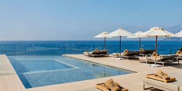 a pool with umbrellas and lounge chairs by the ocean