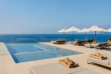 a pool with umbrellas and lounge chairs by the ocean