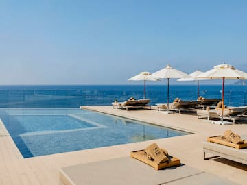 a pool with umbrellas and lounge chairs by the ocean