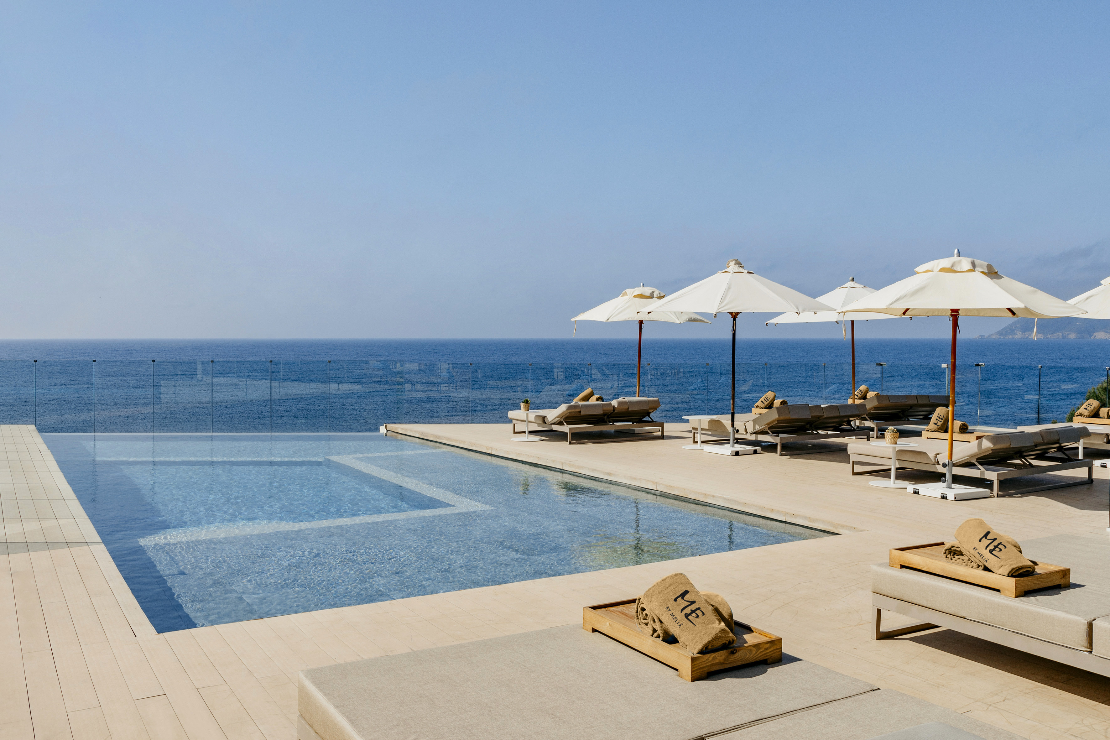 a pool with umbrellas and lounge chairs by the ocean