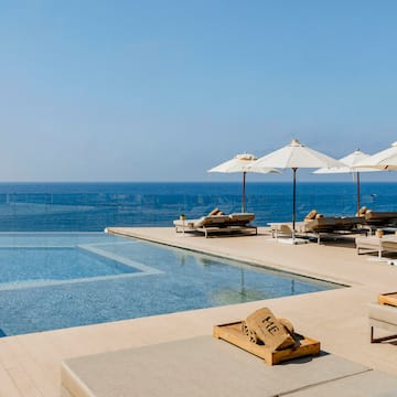 a pool with umbrellas and lounge chairs by the ocean