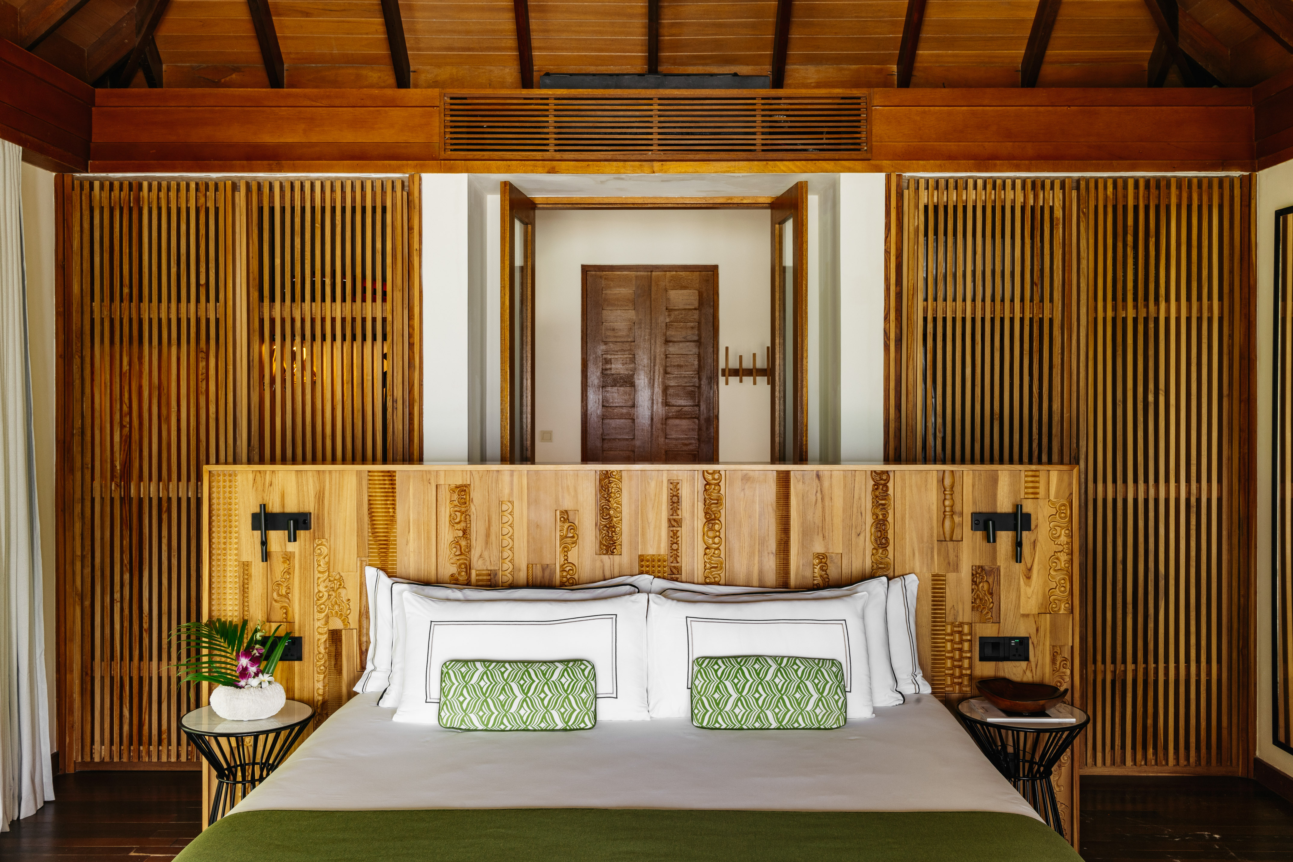 Luxury tropical bedroom, carved wooden headboard, green accents.