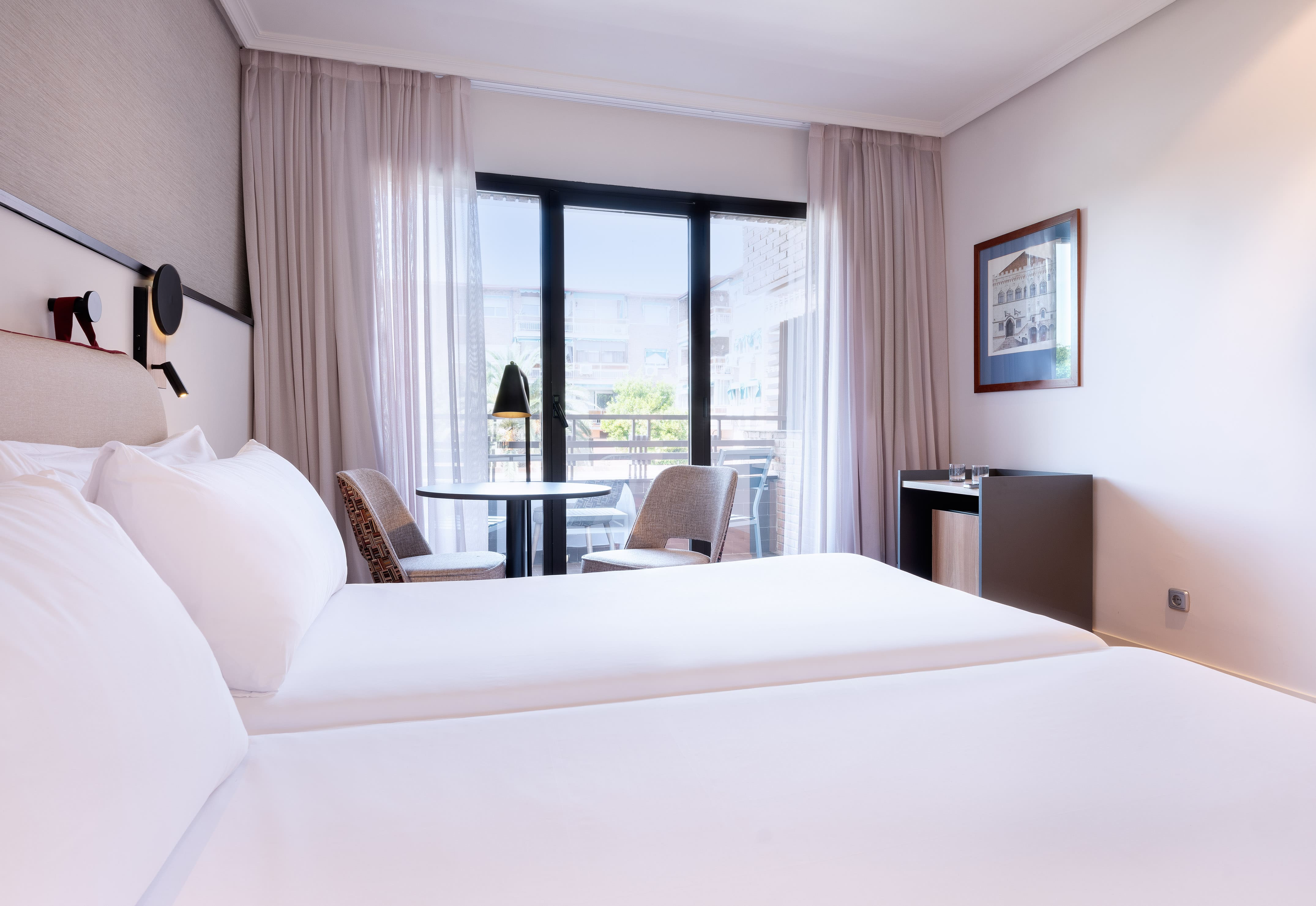 Modern hotel room with two single beds, balcony, and bright neutral decor.