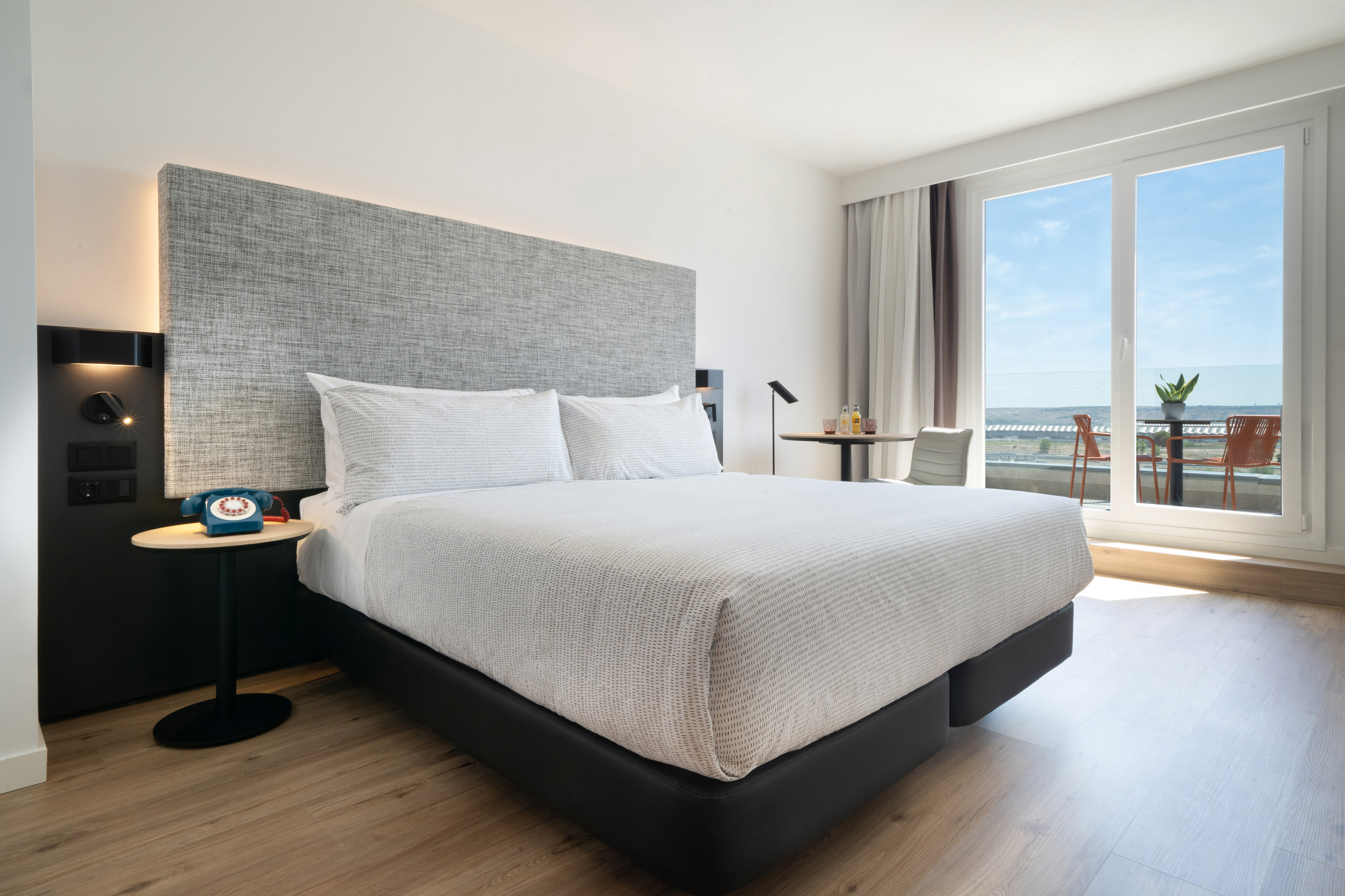 Bright, modern hotel room with king bed, wood floor, balcony, and scenic view.