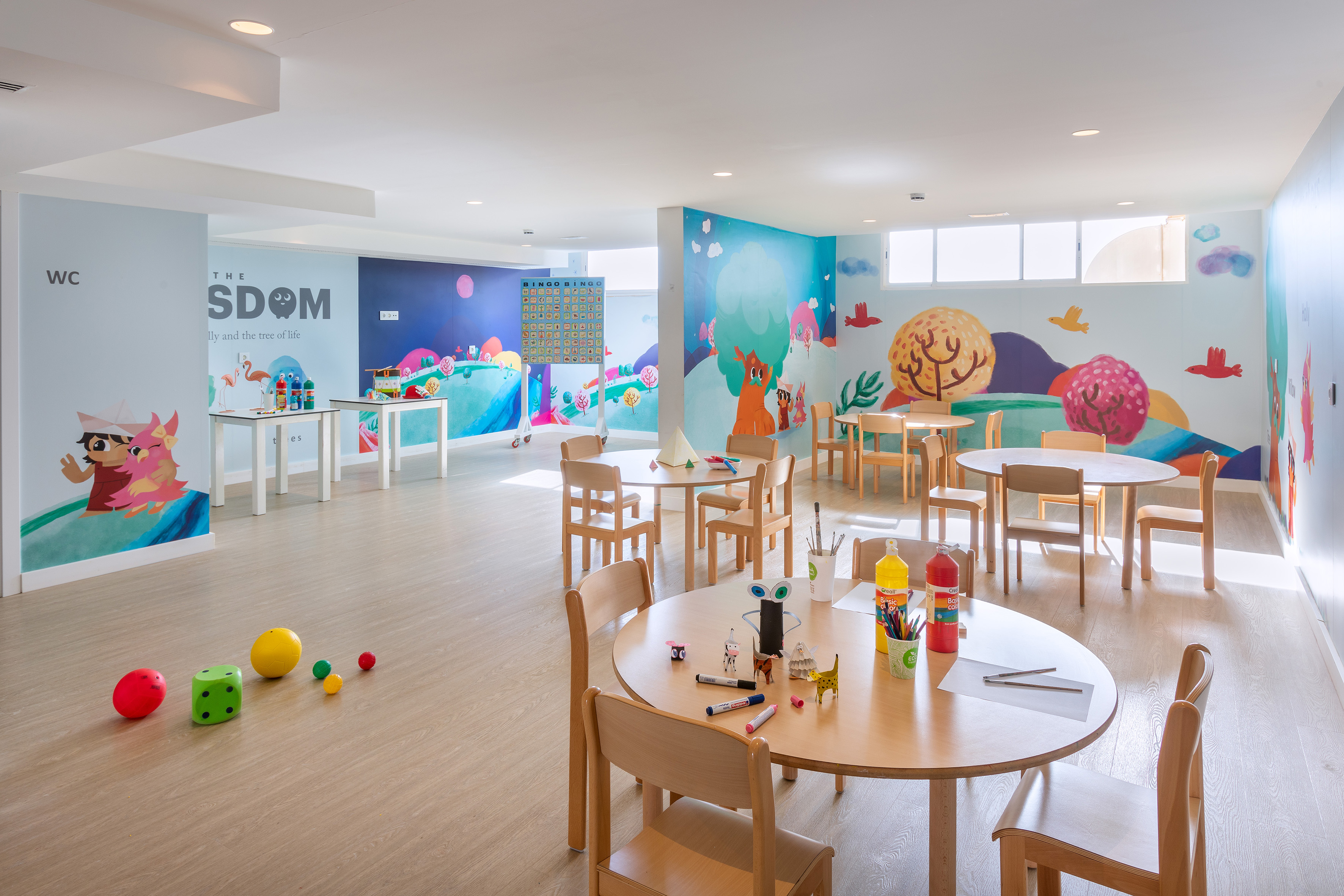 Kids' activity room with colorful murals, small wooden tables, and art supplies.