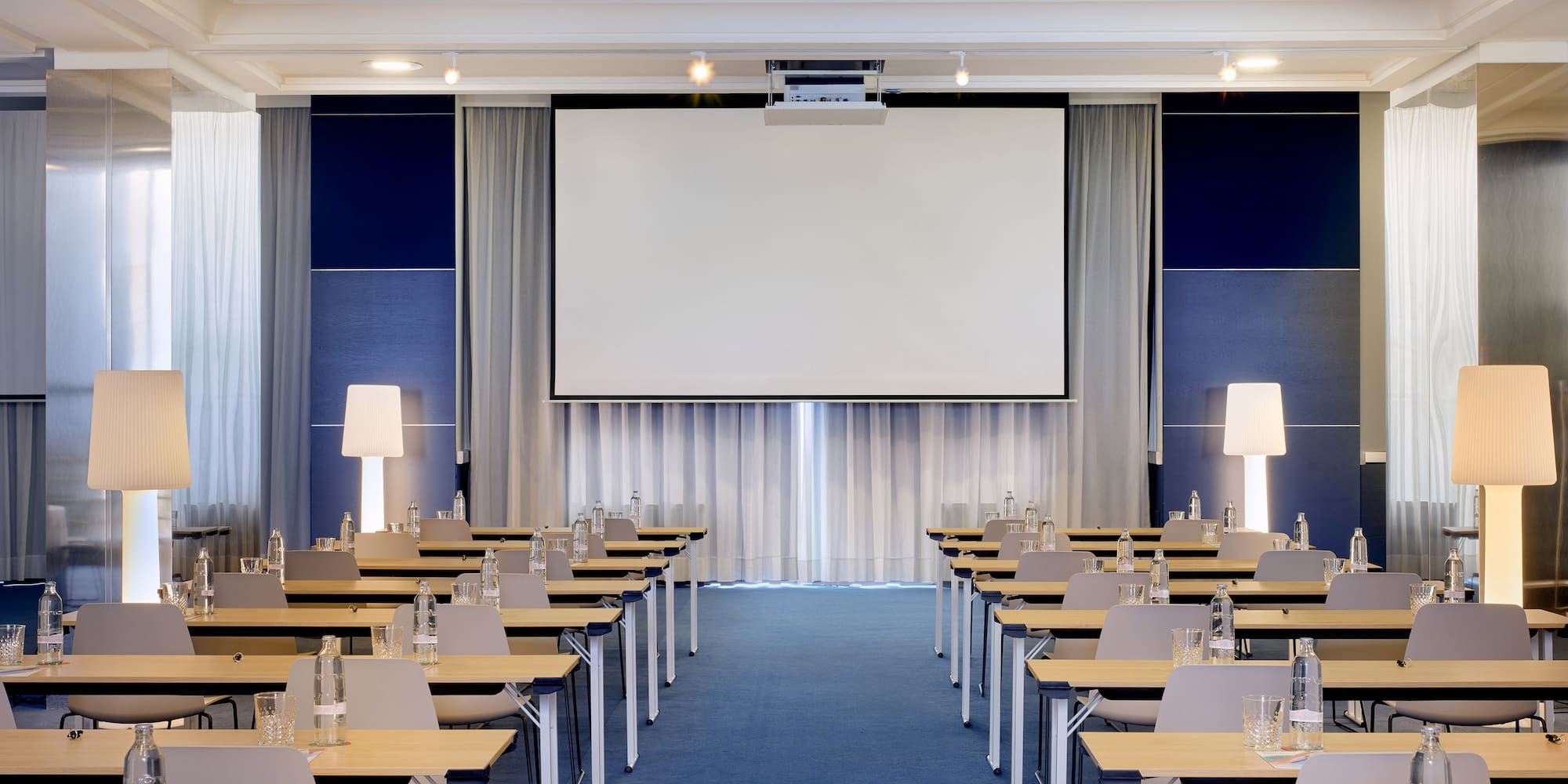 Sala de conferencias equipada con proyector, mesas y alfombra azul.