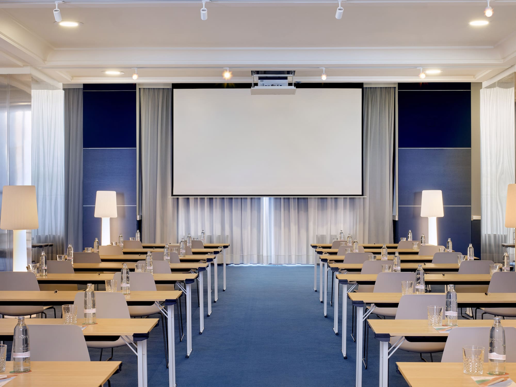 Sala de reuniones corporativa con pantalla, mesas, sillas y alfombra azul.