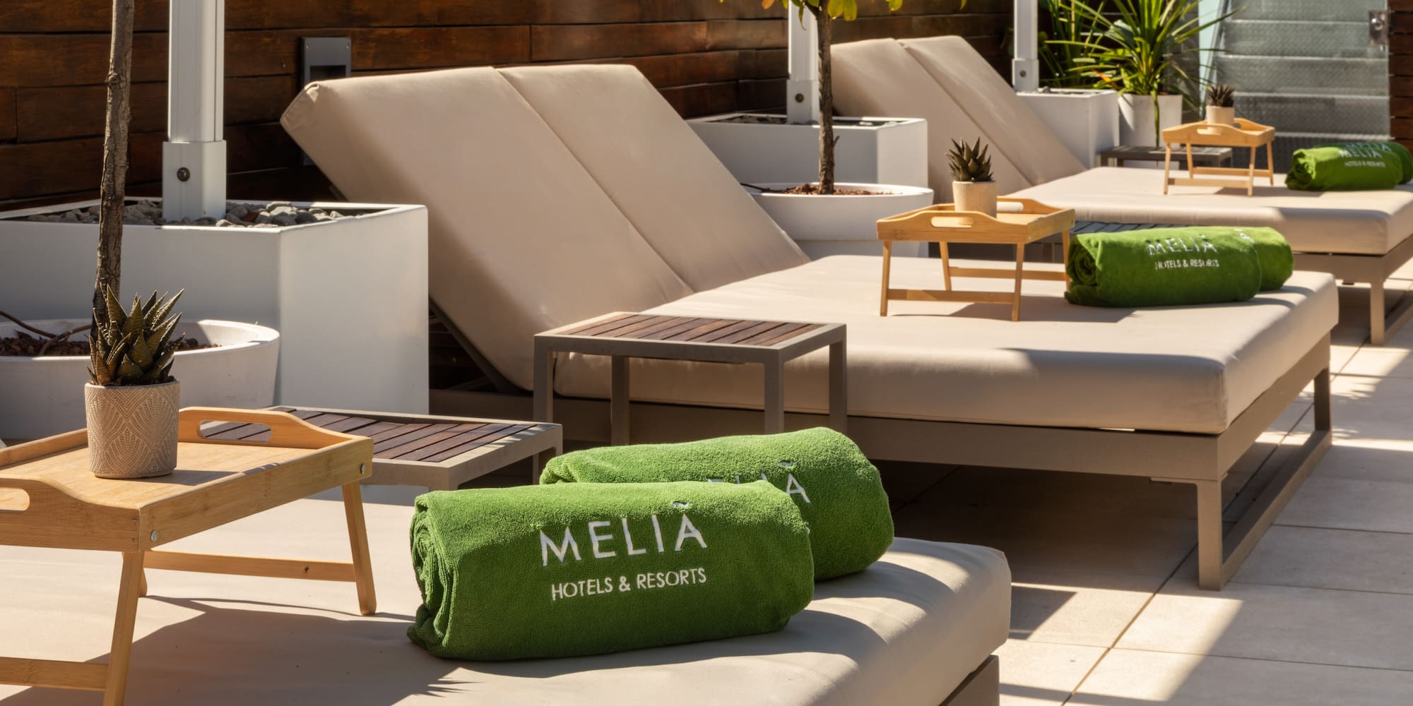 Meliá Hotels & Resorts sun loungers with green towels on a sunny rooftop terrace.