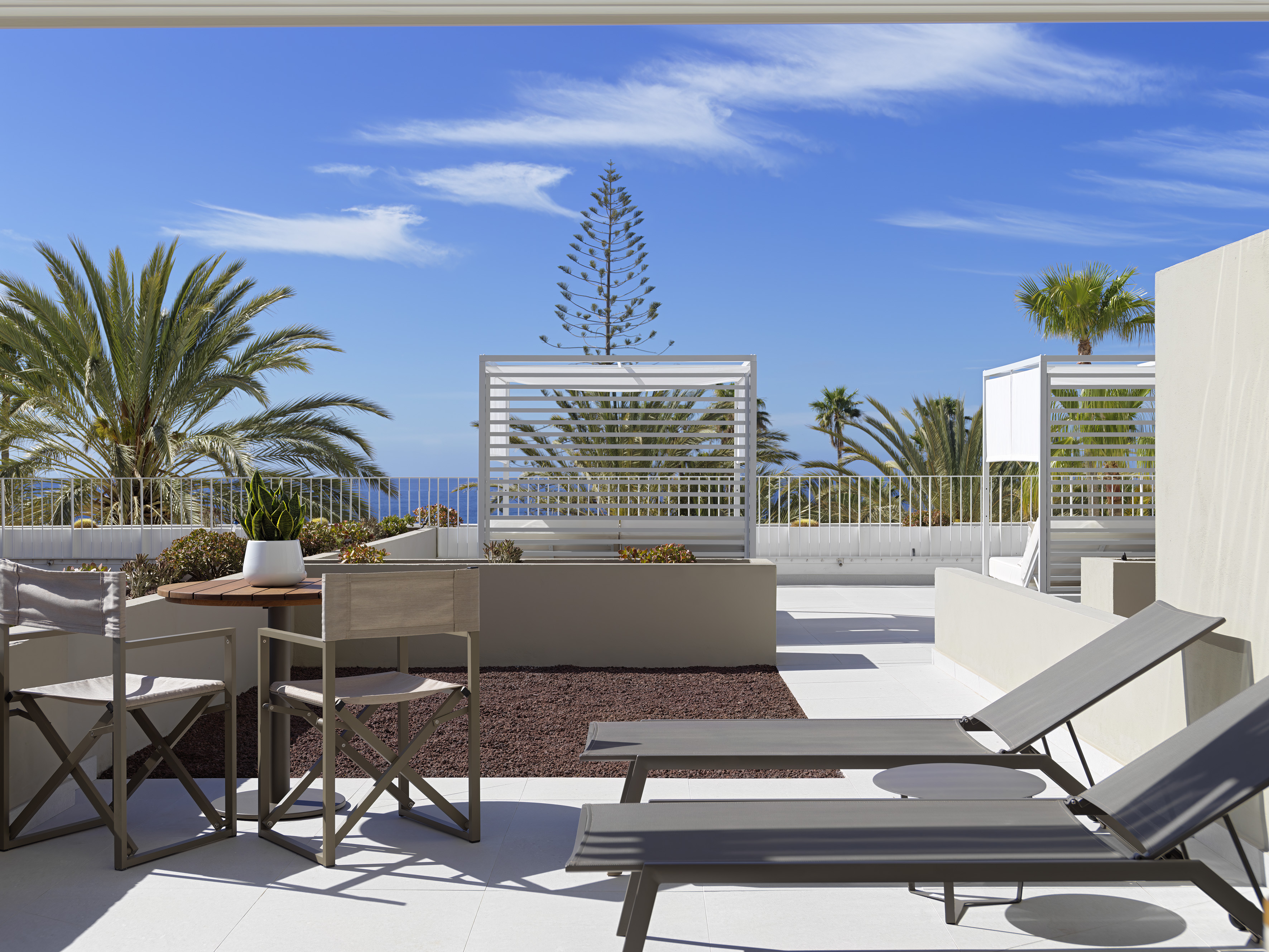 Modern terrace: Ocean view, palm trees, sun loungers, outdoor seating.