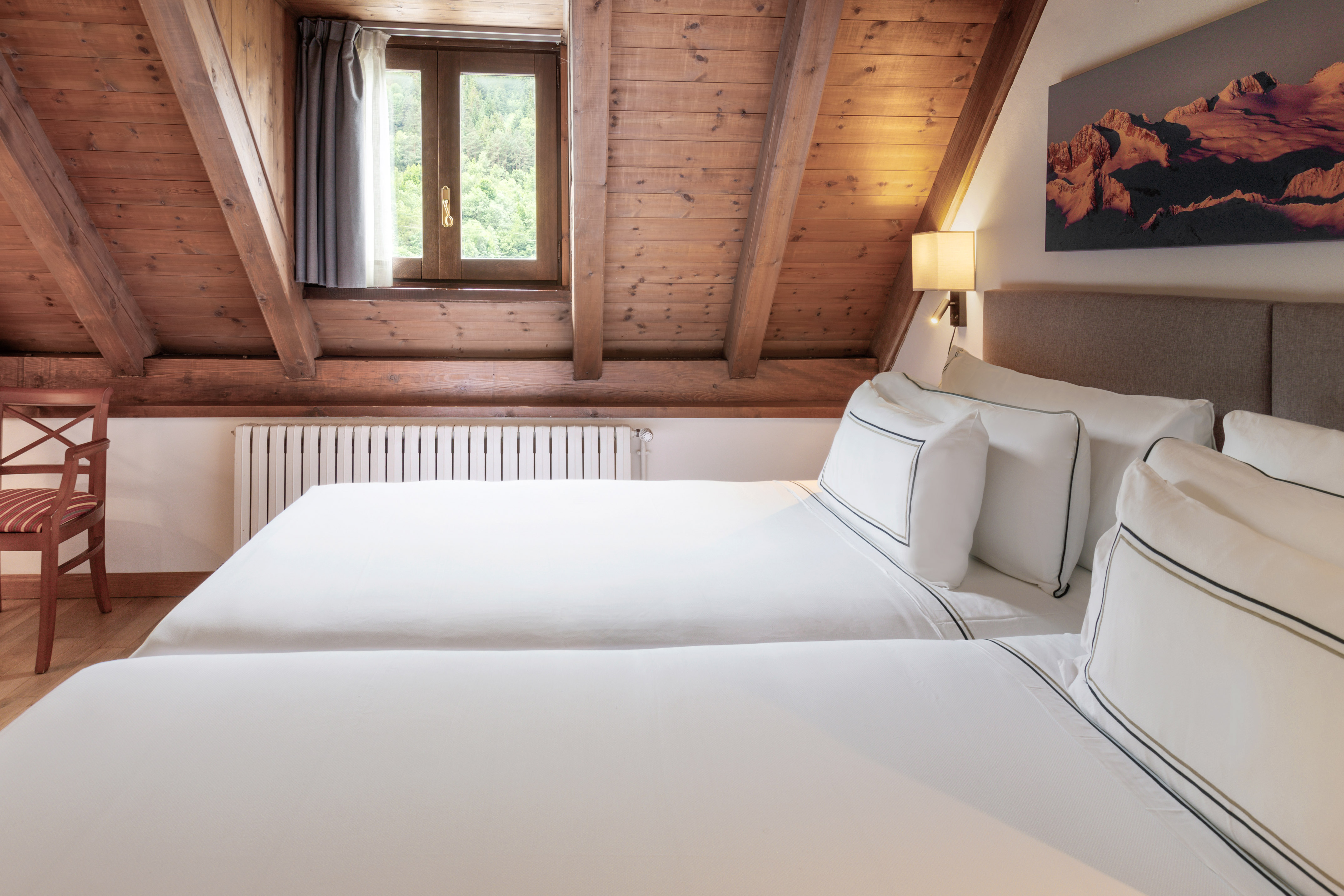 Attic hotel room with two beds, wooden ceiling beams, window, and wall art.