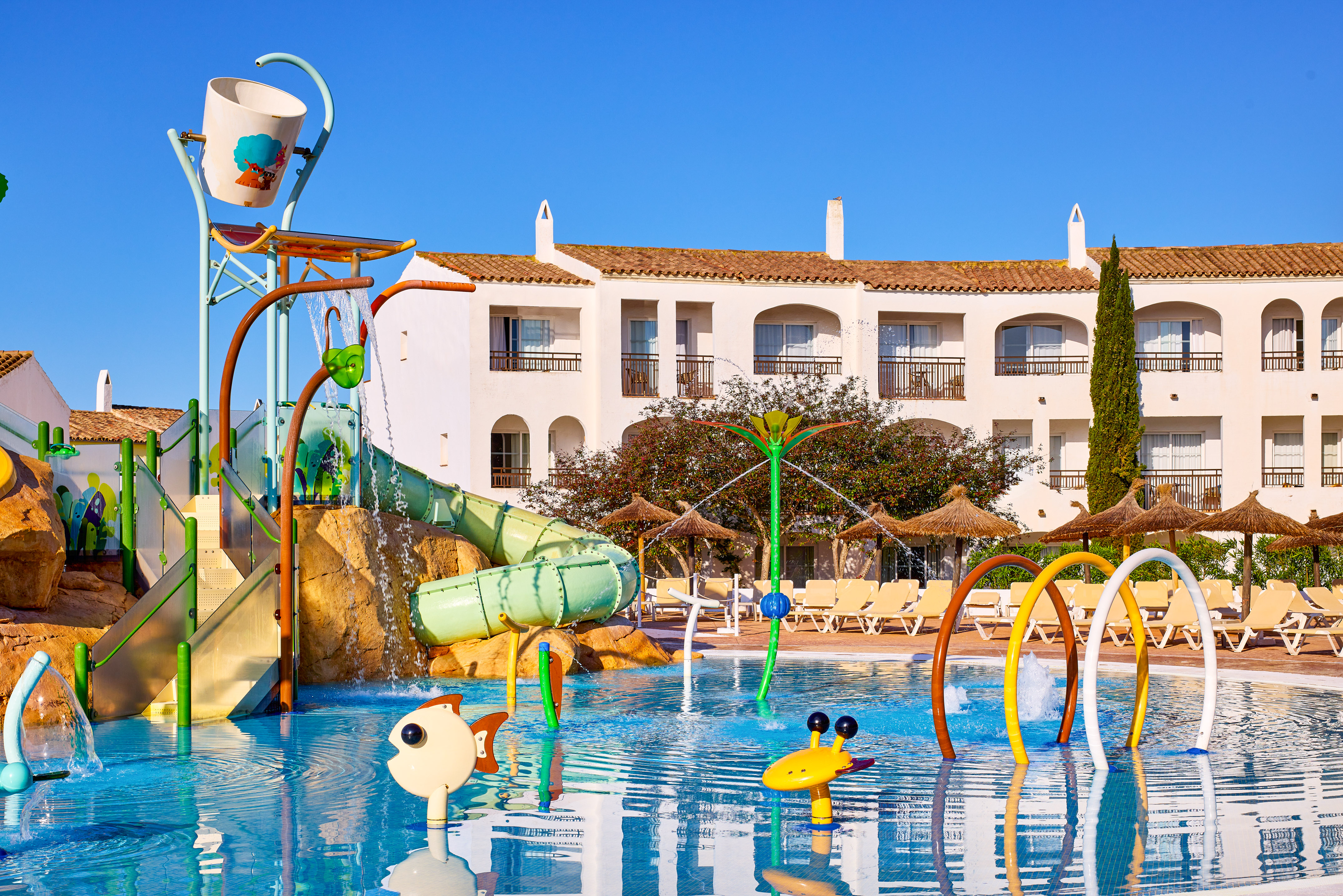 Sunny resort water park with colorful slides, splash zone, pool, and hotel.