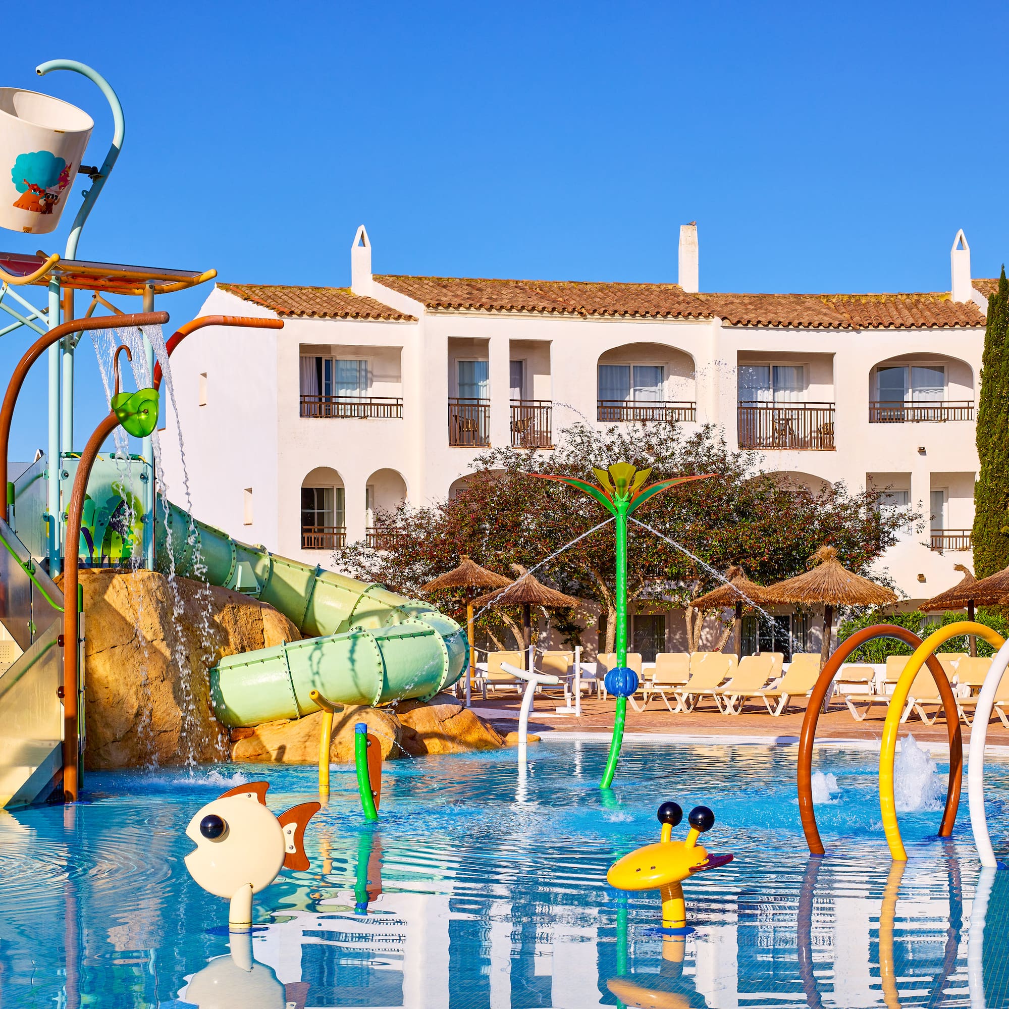 Sunny resort water park with colorful slides, splash zone, pool, and hotel.