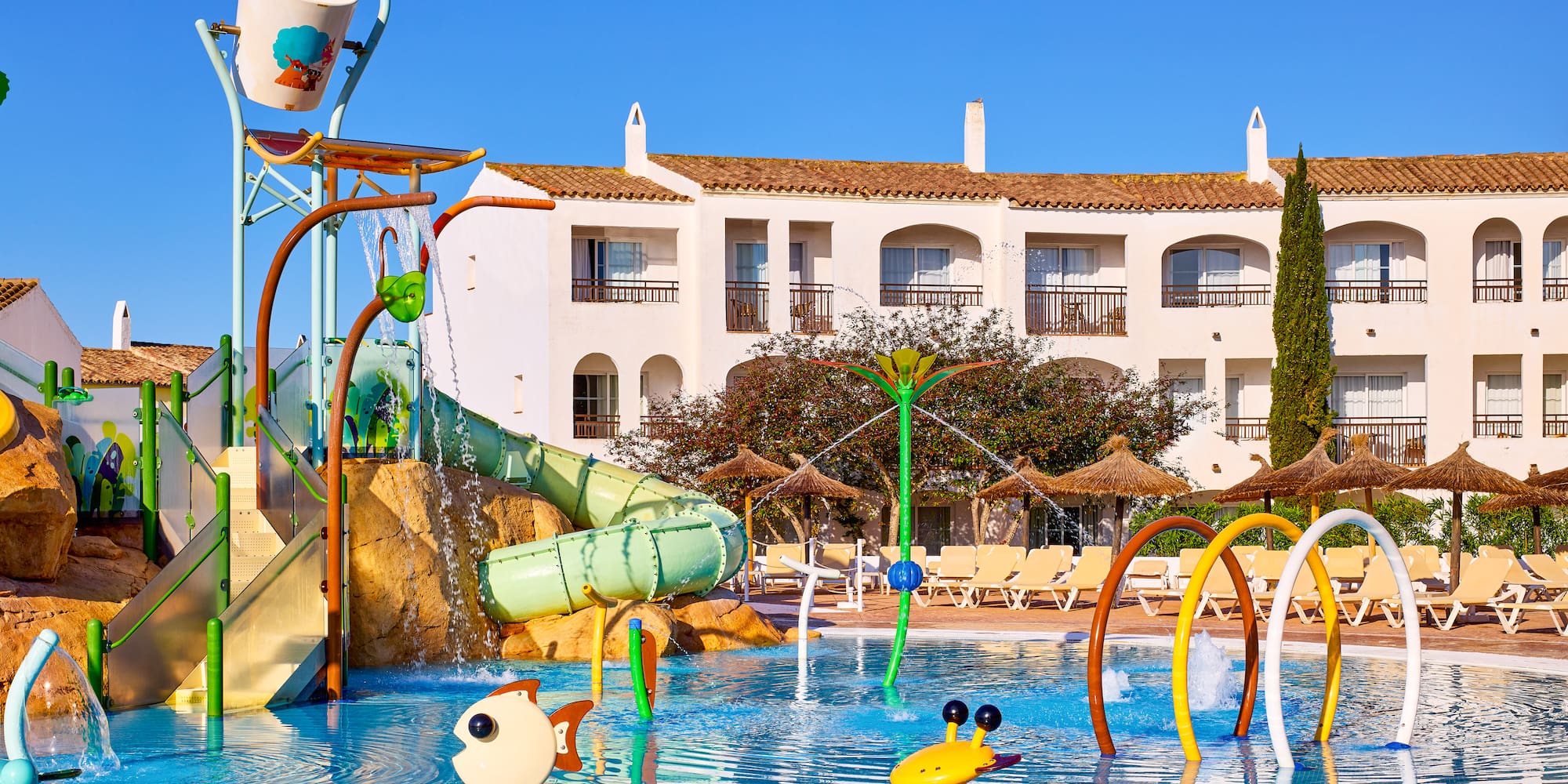 Sunny resort water park with colorful slides, splash zone, pool, and hotel.