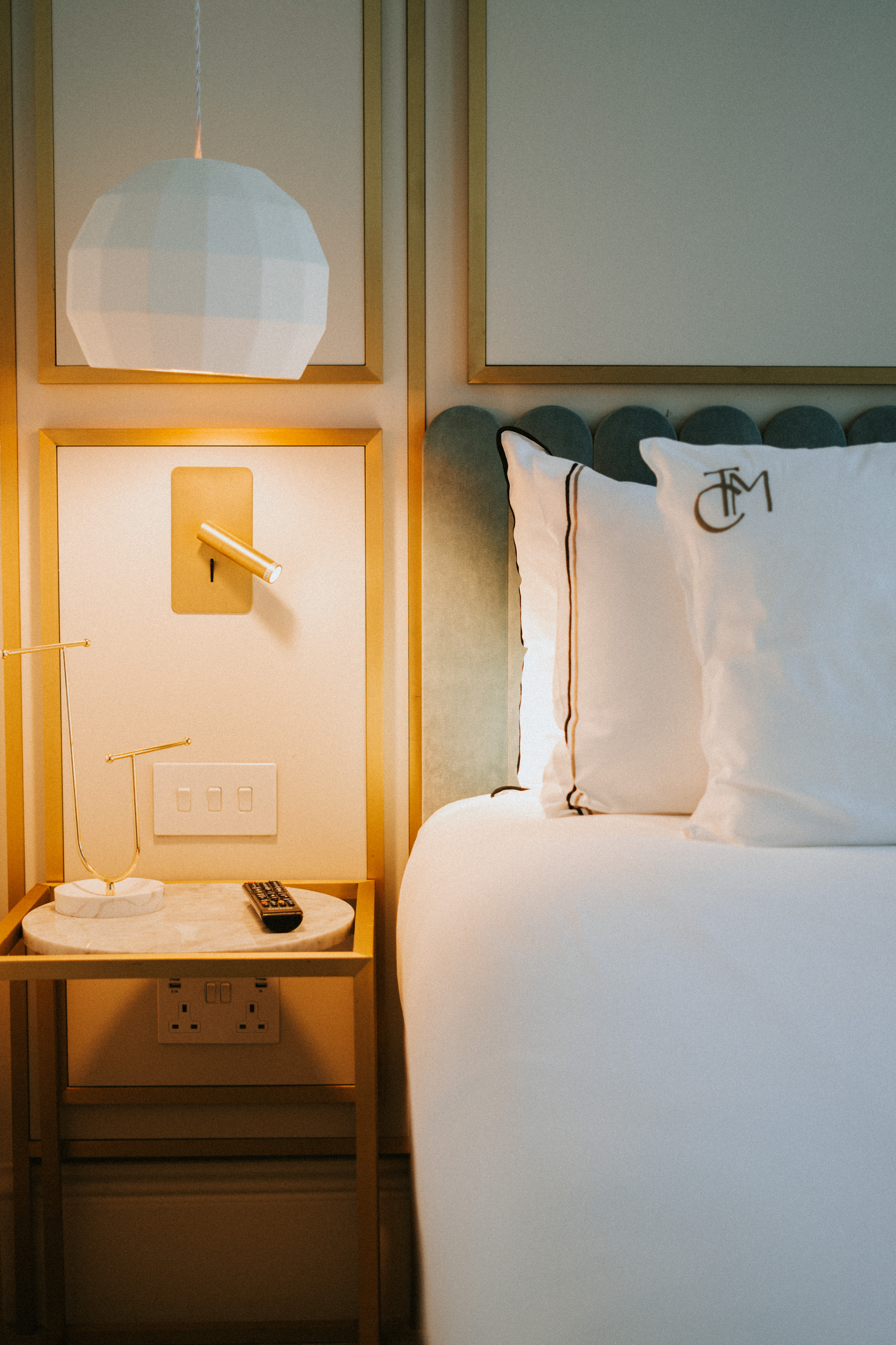Elegant hotel bedroom: white bed, gold decor, marble nightstand, reading lamp.