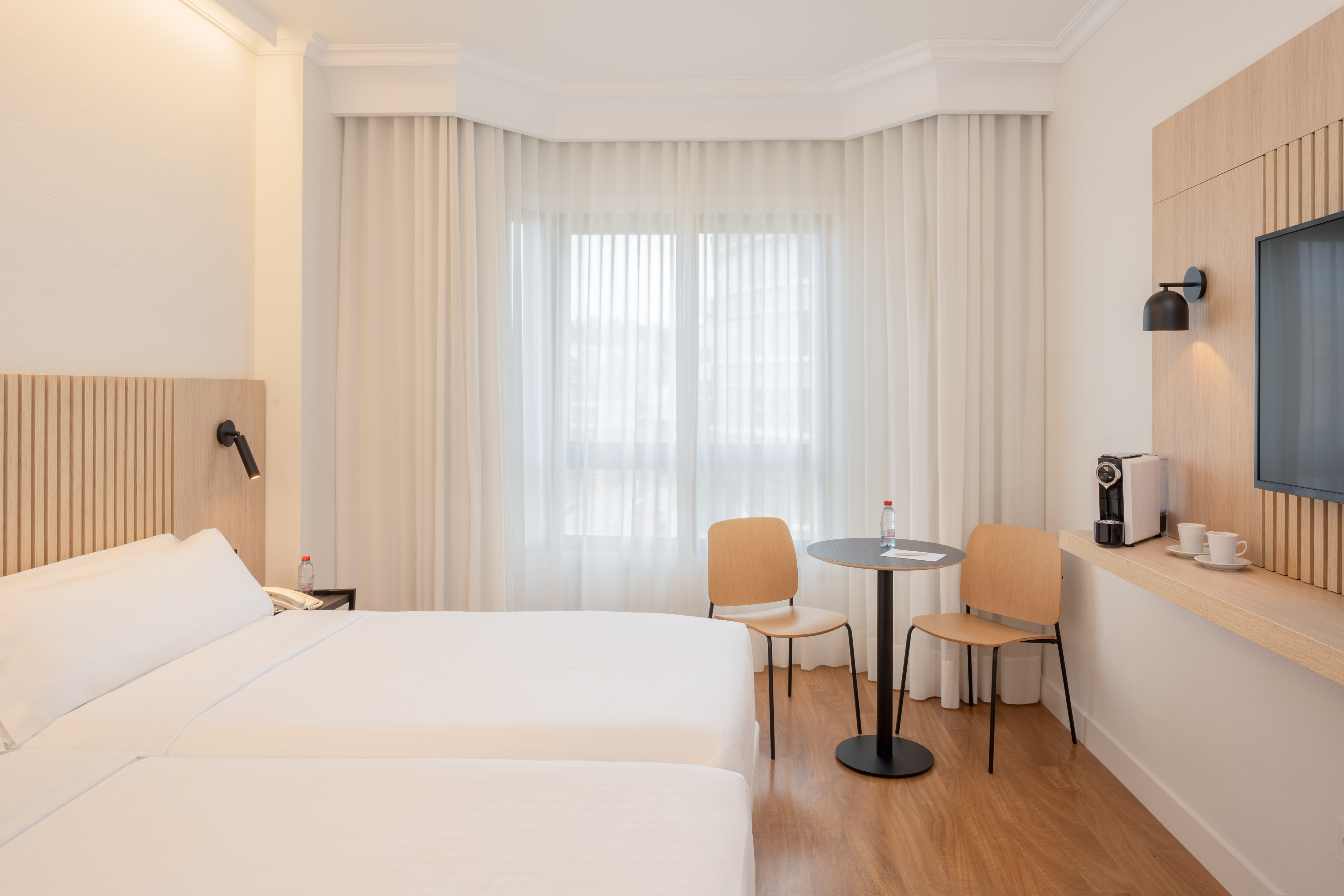 Bright hotel room with twin beds, modern design, window, and coffee machine.