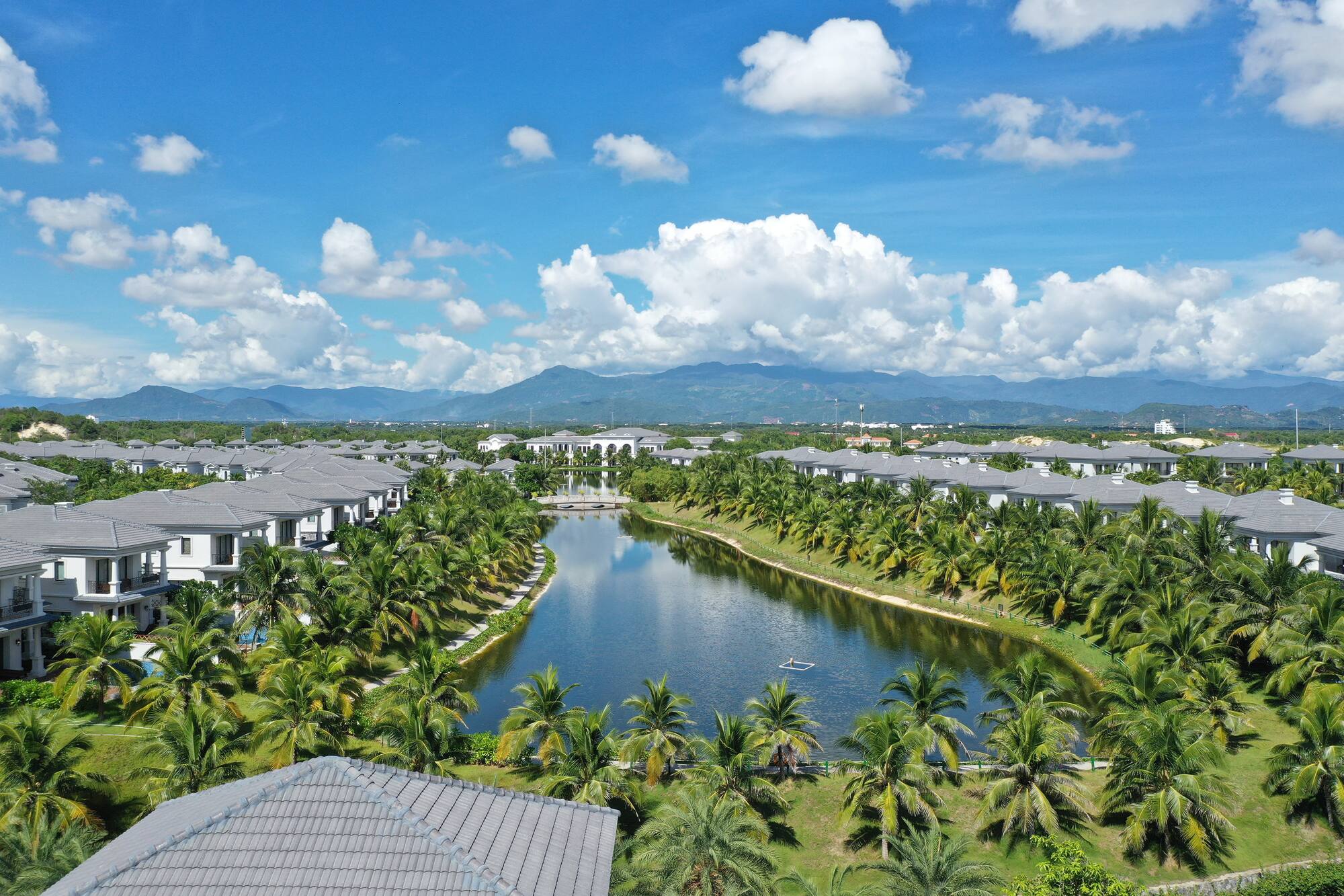 Overhead view of tropical resort, lake, palm-lined villas, and mountains.