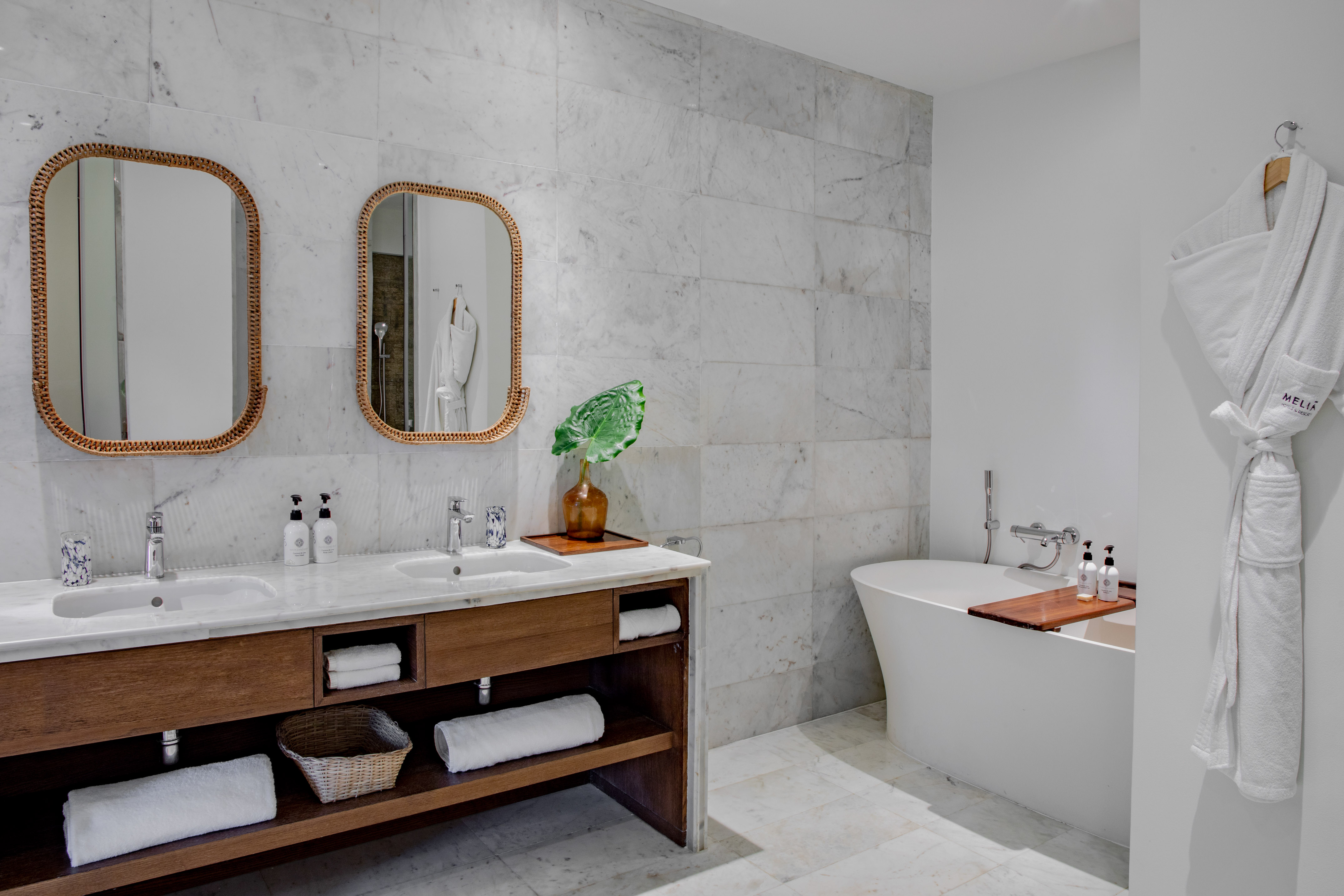 Luxury marble bathroom with double vanity, rattan mirrors, and freestanding tub.