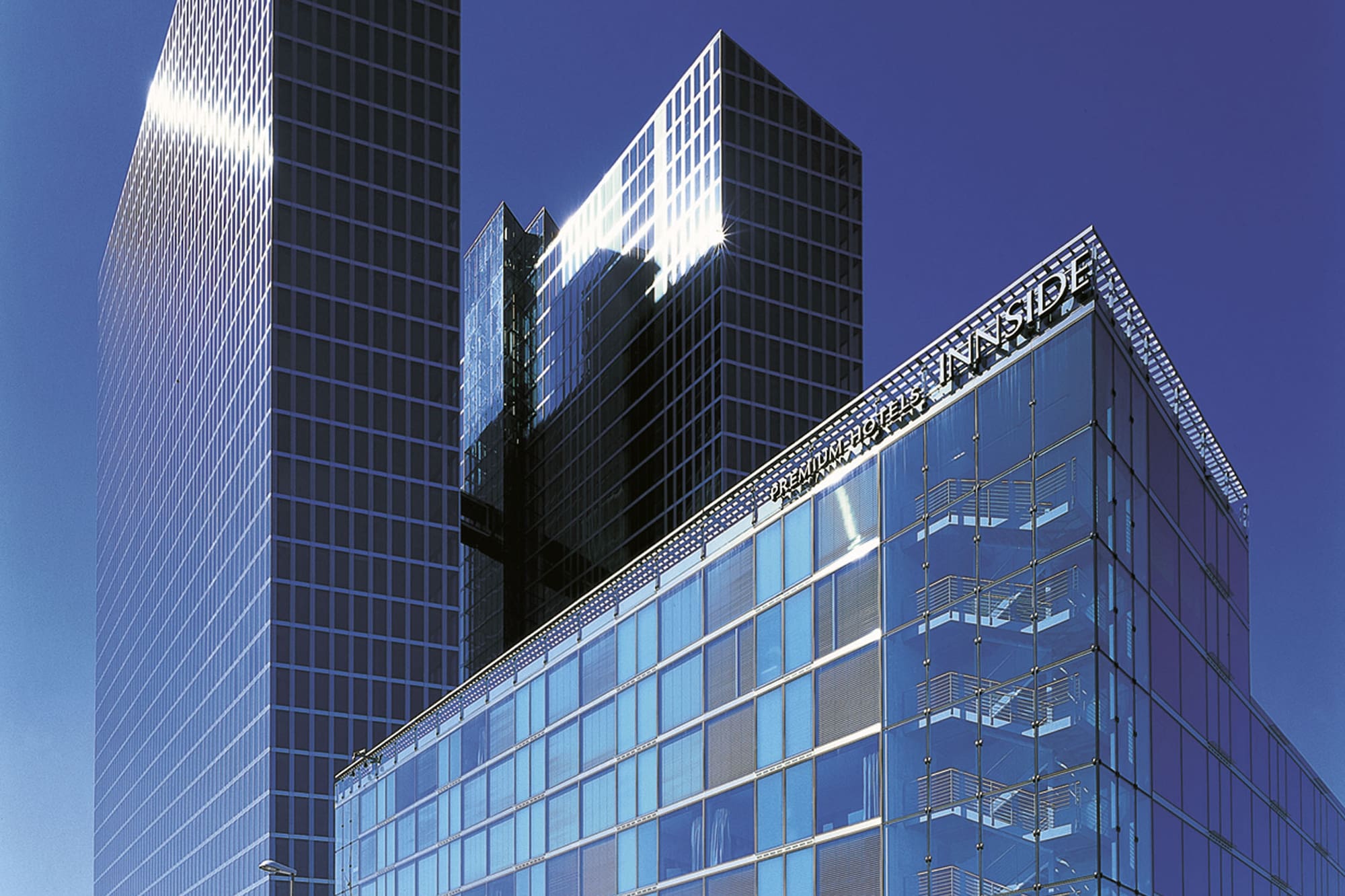 Modern glass skyscrapers and Innside hotel building under clear blue sky.