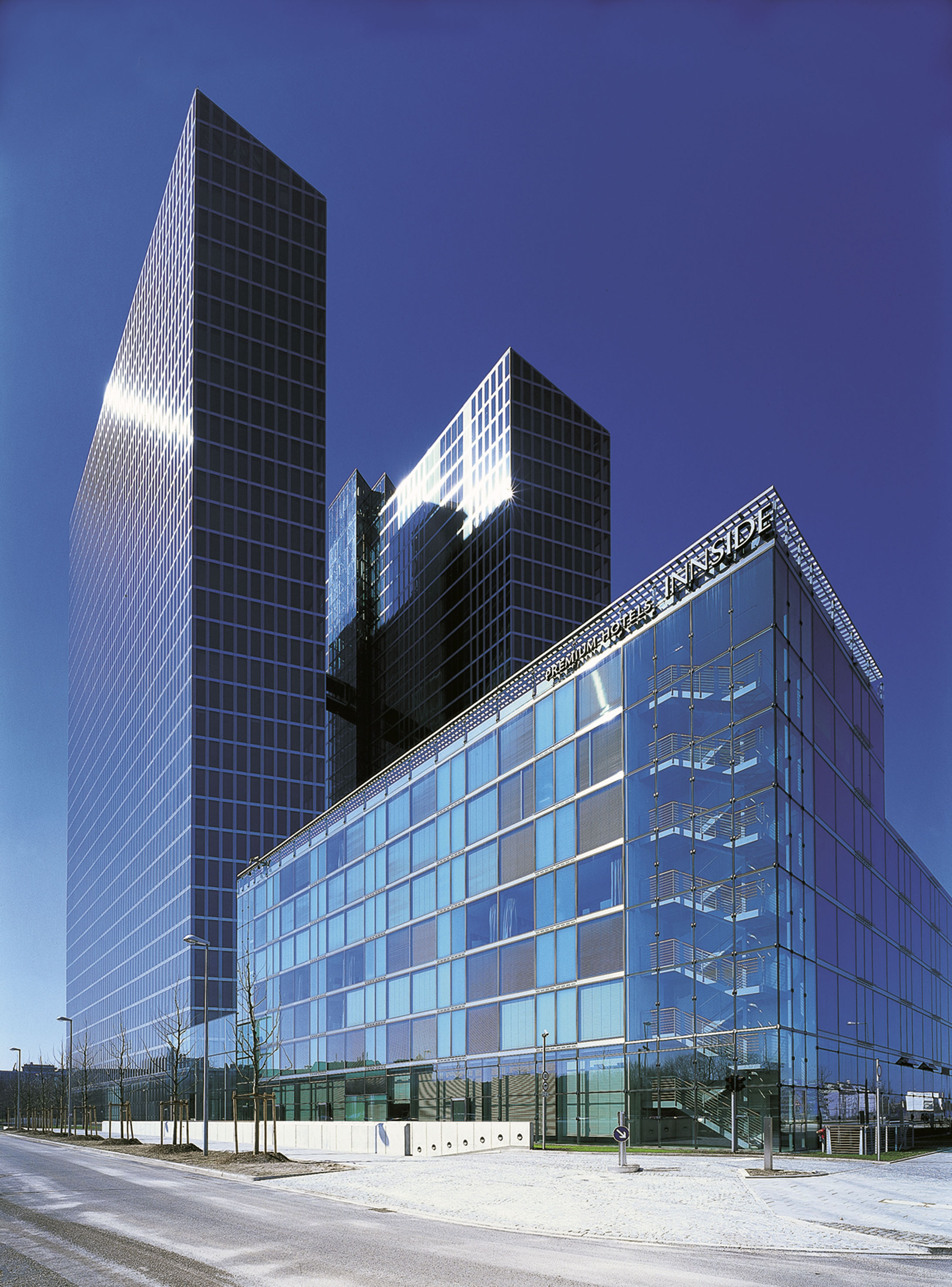 Modern glass skyscrapers and Innside hotel building under clear blue sky.