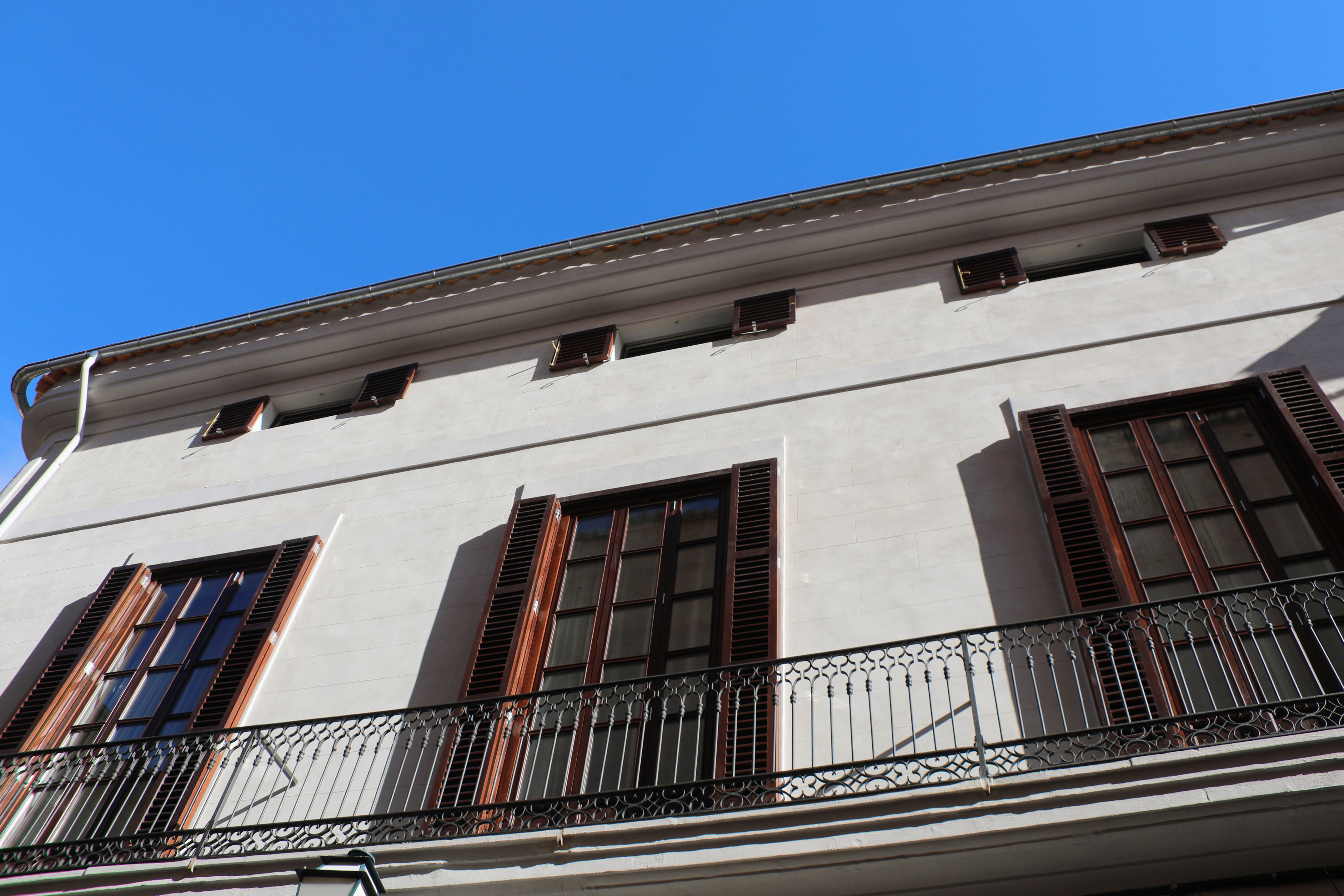 Building facade with dark wooden shutters, ornate balcony, and blue sky.