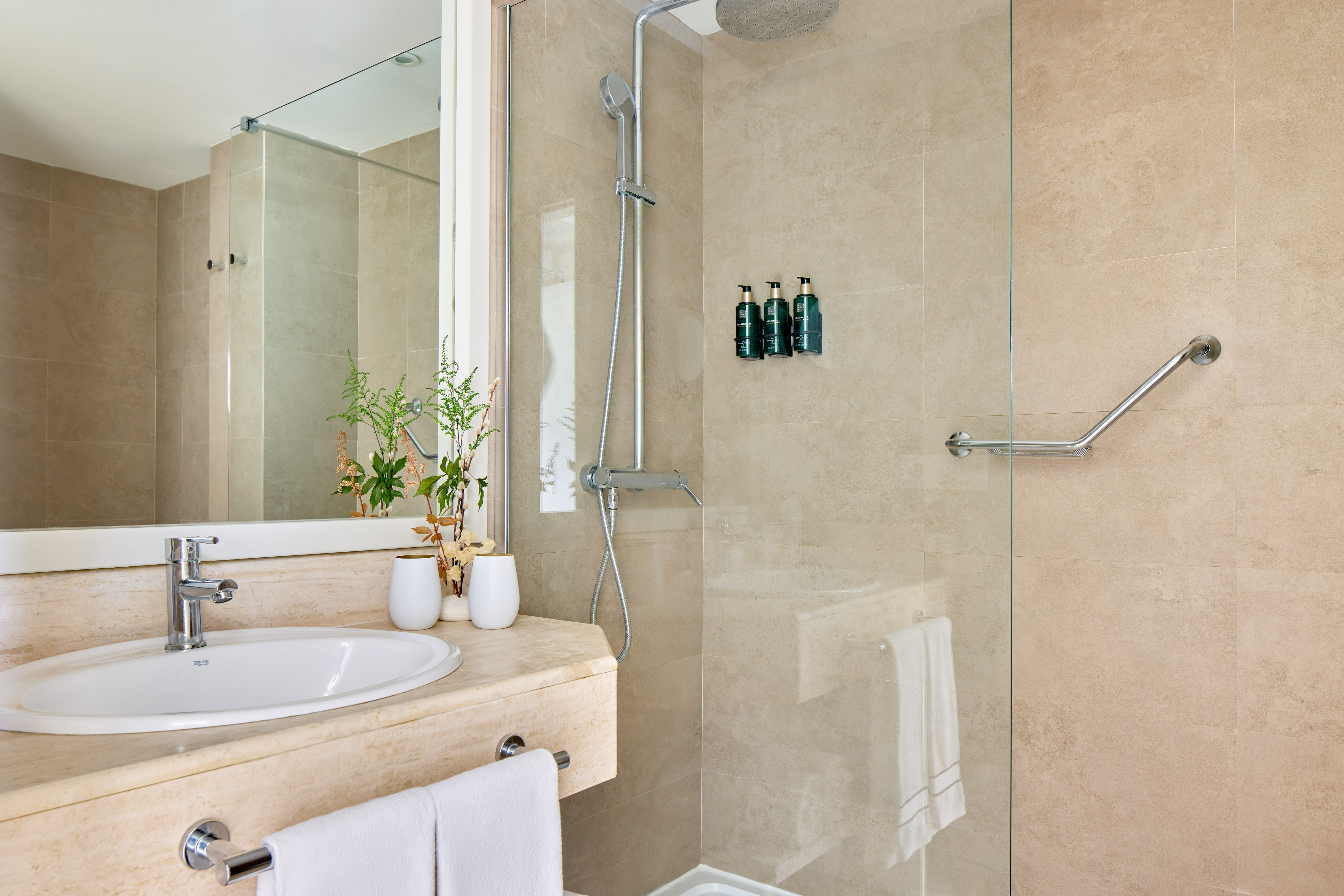 Beige tiled bathroom with contemporary sink, mirror, and accessible shower.