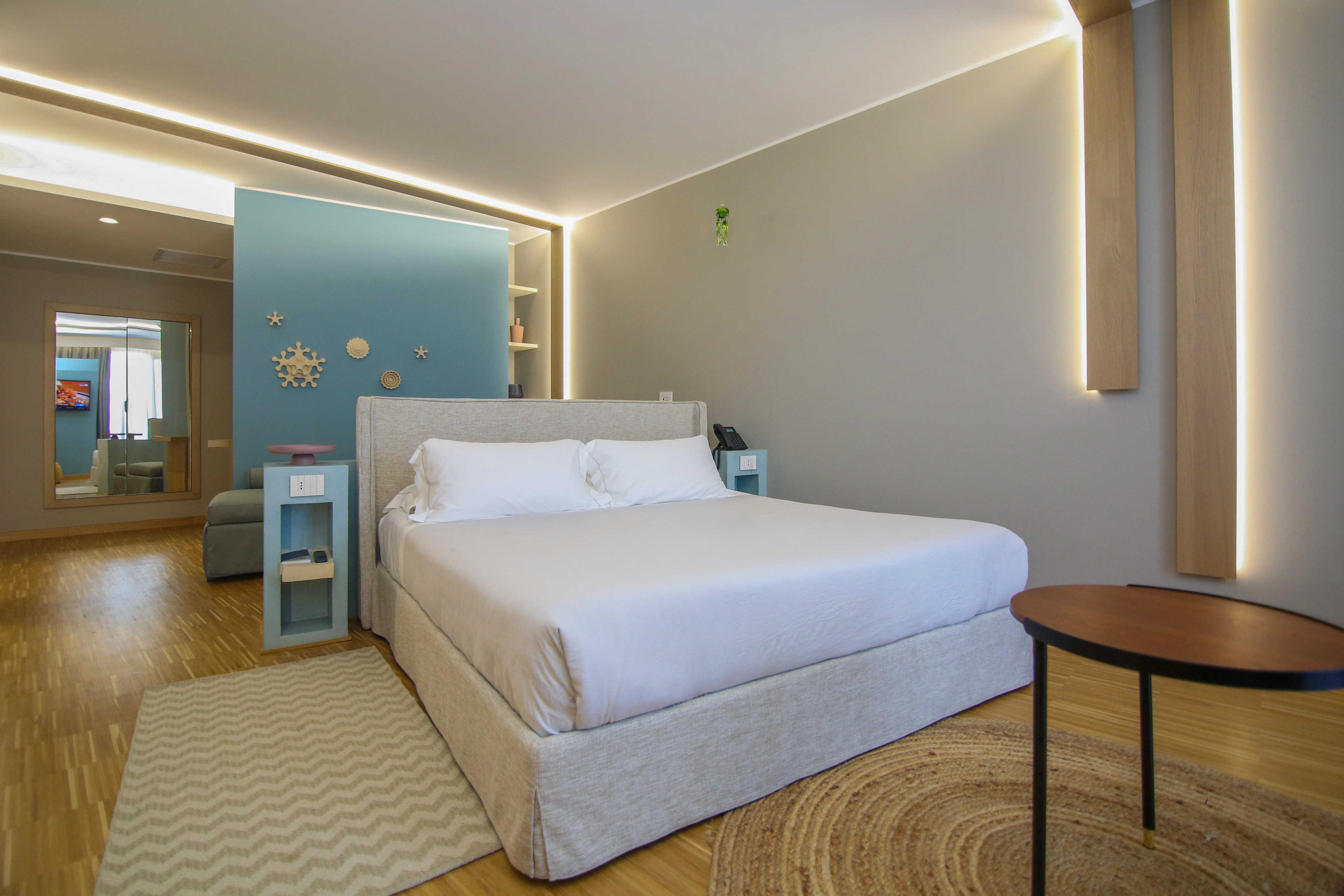 Modern hotel room with king bed, blue accent wall, and wooden floor.