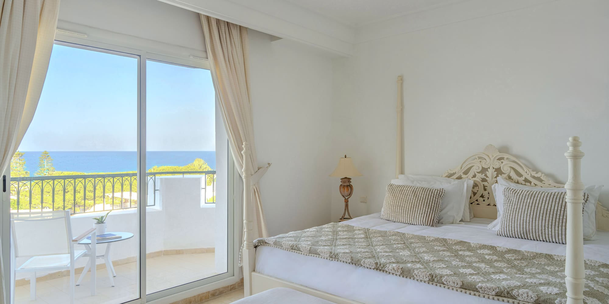 Bright bedroom with balcony, ocean view, and large bed.