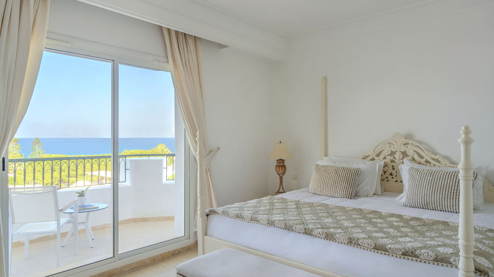 Bright bedroom with balcony, ocean view, and large bed.