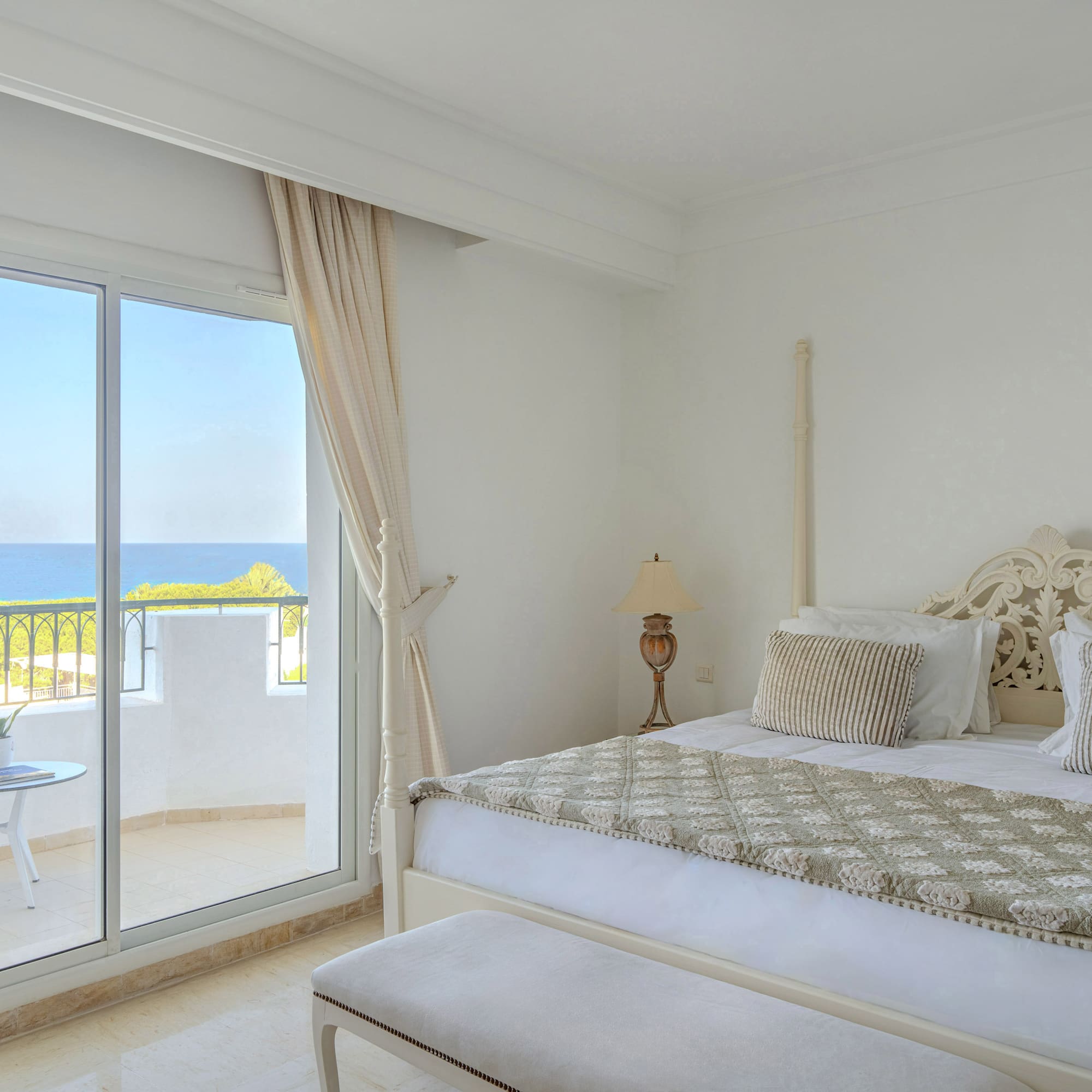 Bright bedroom with balcony, ocean view, and large bed.