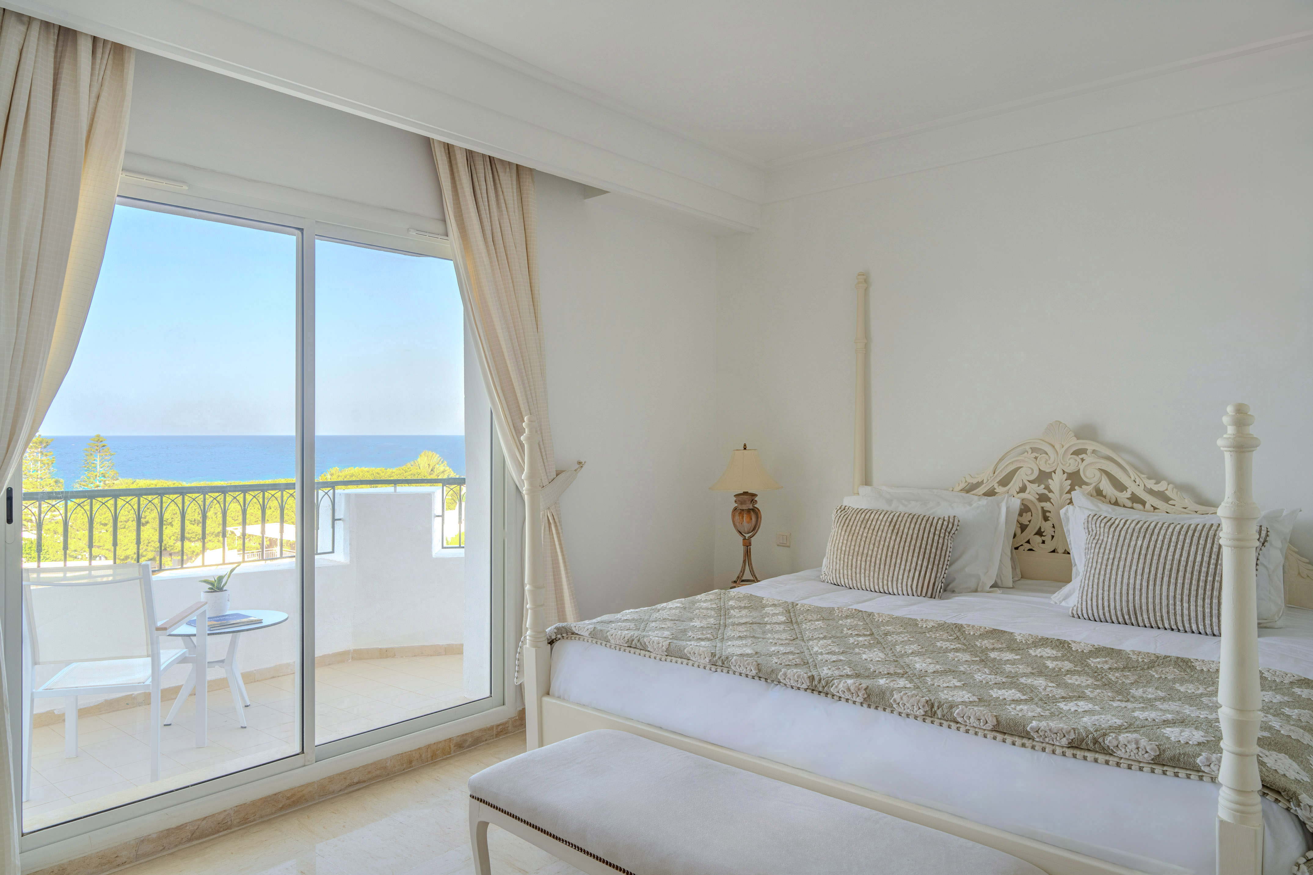 Bright bedroom with balcony, ocean view, and large bed.