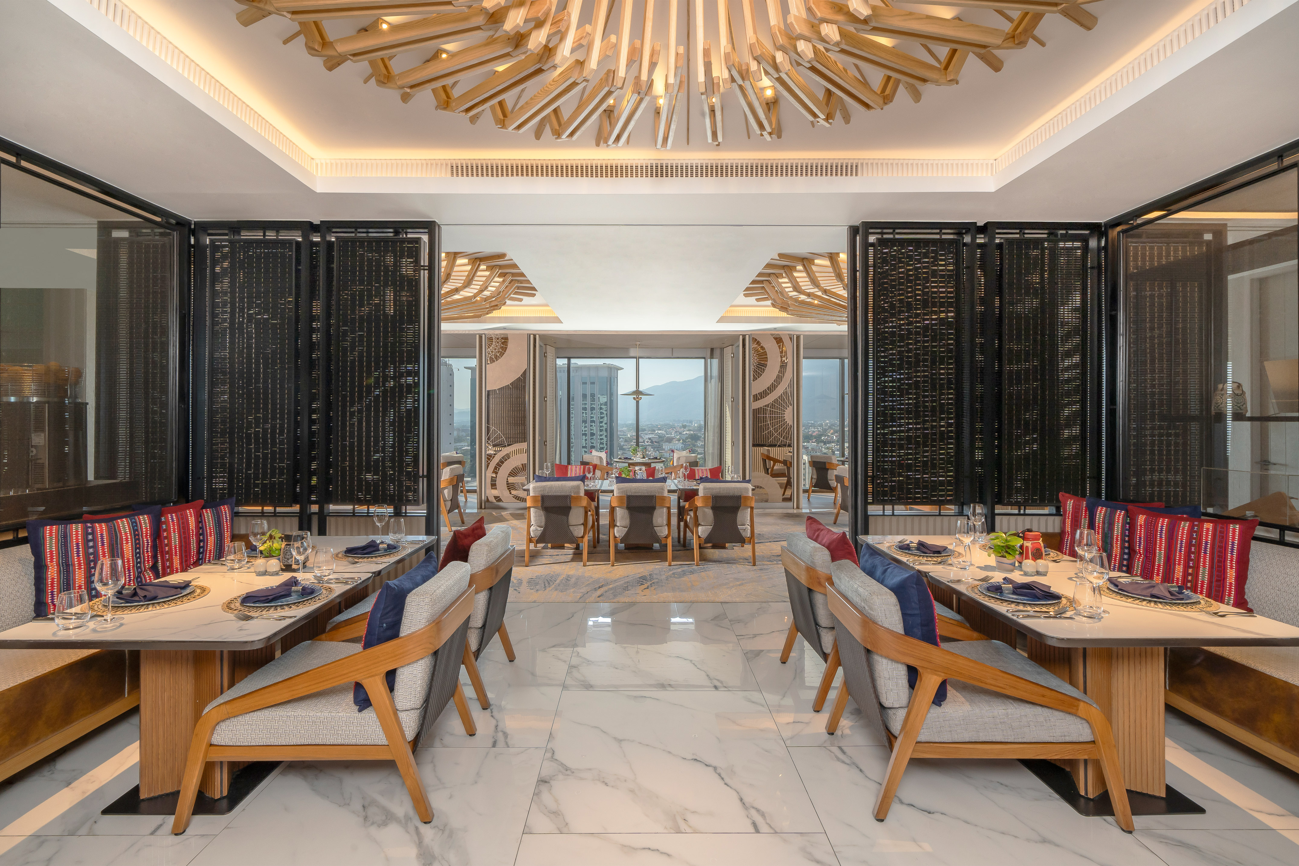 Modern luxury restaurant with city view, set tables, and unique wood chandelier.