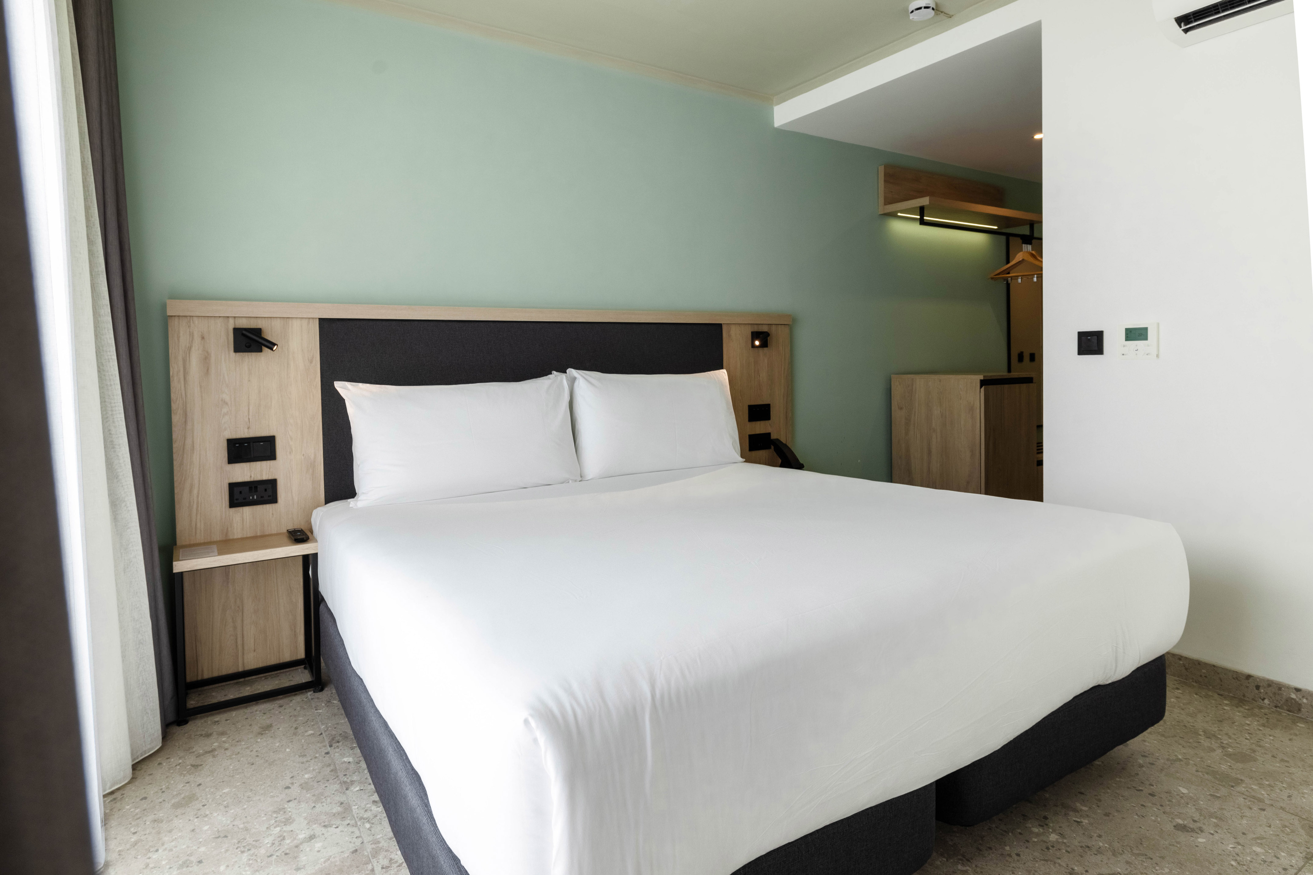 Modern hotel room with white bed, wooden headboard, and light green wall.