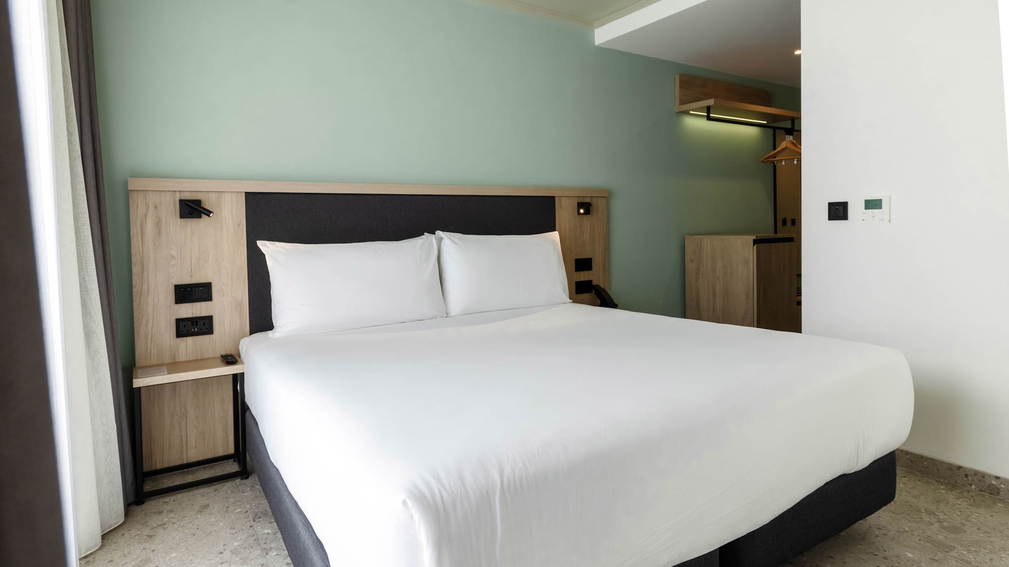 Modern hotel room with white bed, wooden headboard, and light green wall.