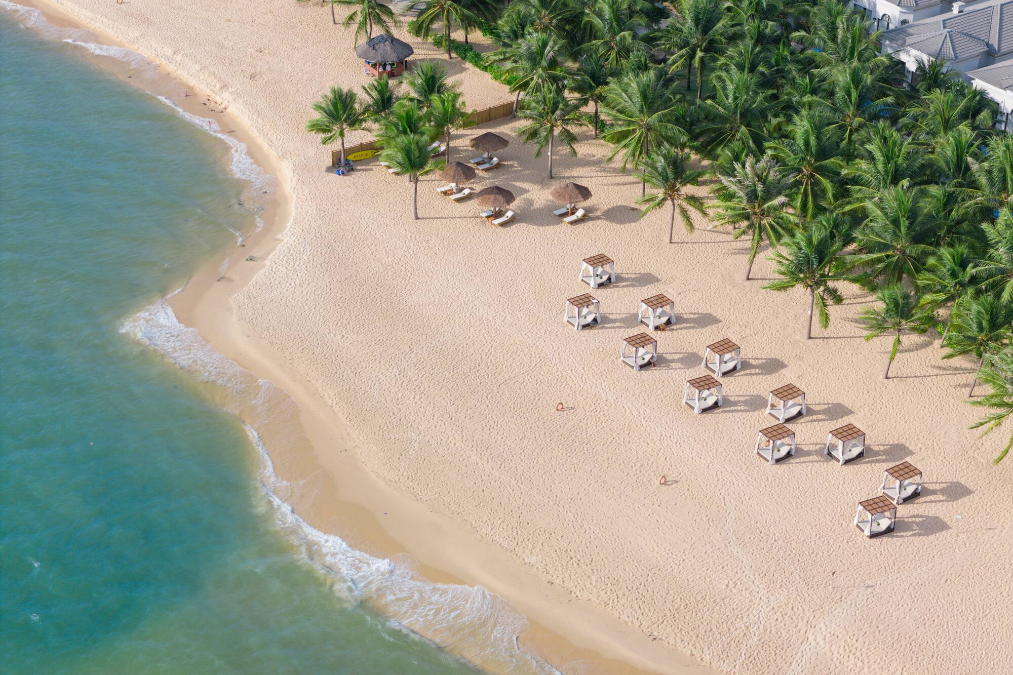 Aerial tropical beach resort with palm trees, cabanas, and turquoise ocean.