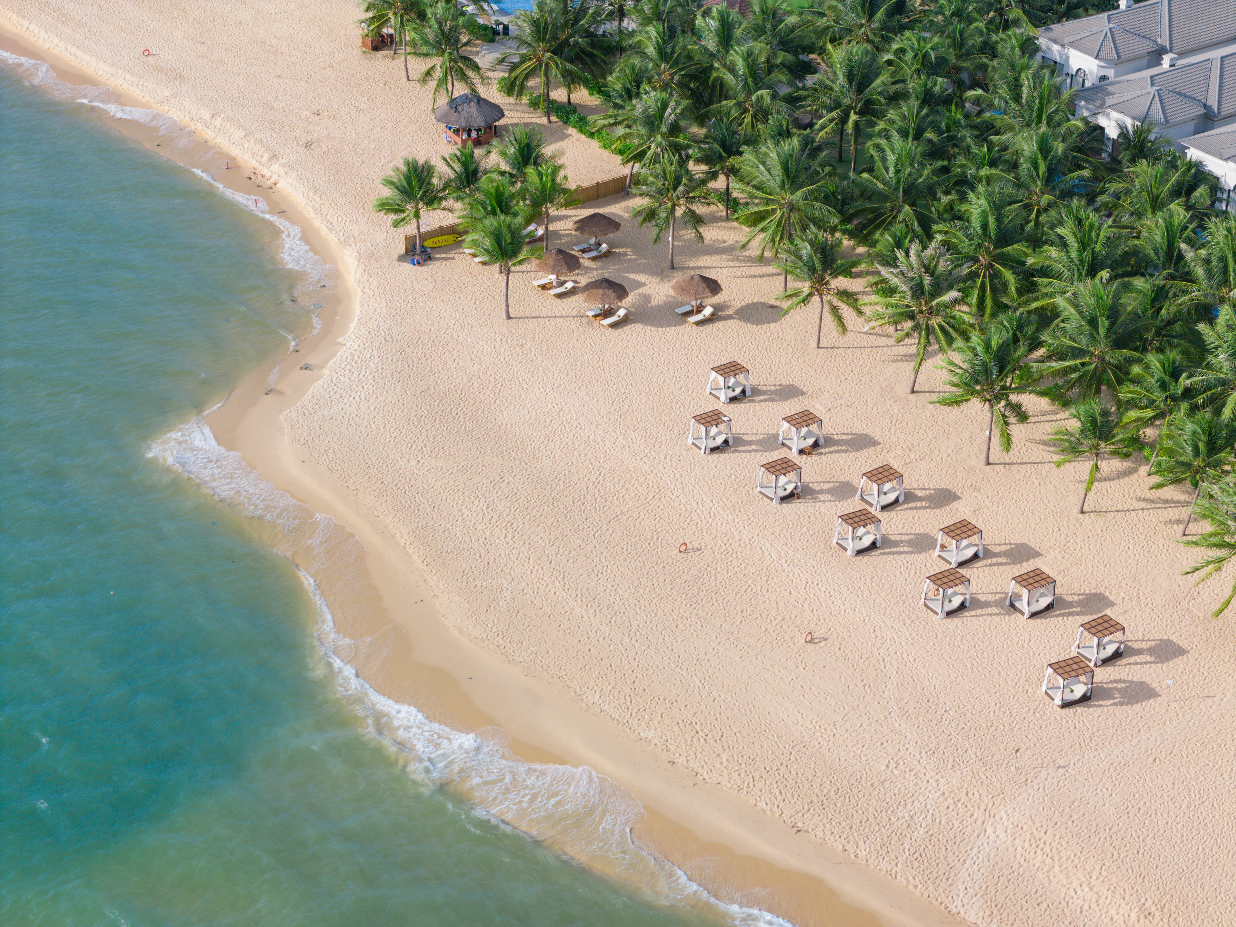 Aerial tropical beach resort with palm trees, cabanas, and turquoise ocean.